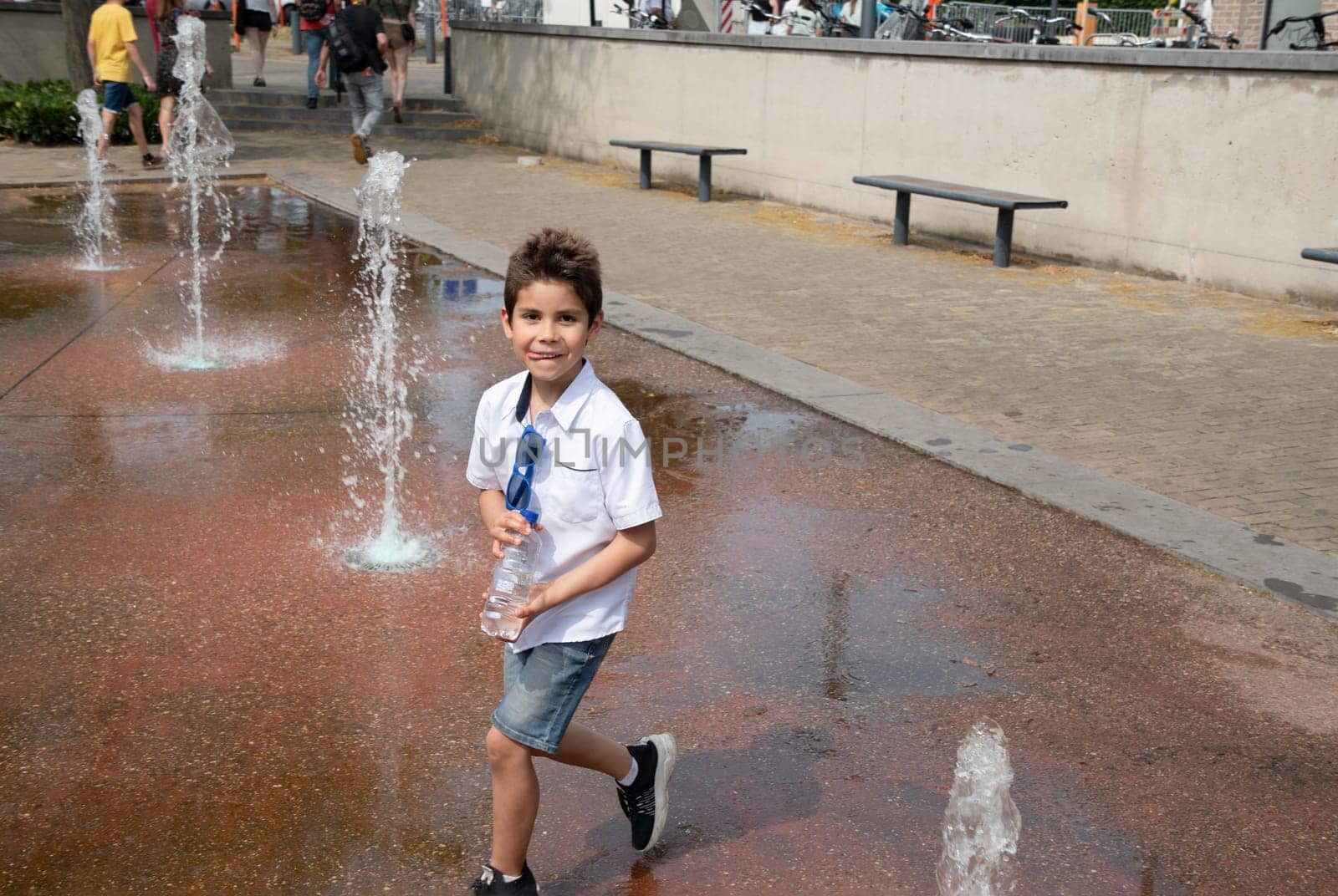 Boy playing with fountain in public park, child having fun, dancing, having fun in hot summer, leisure concept, High quality photo