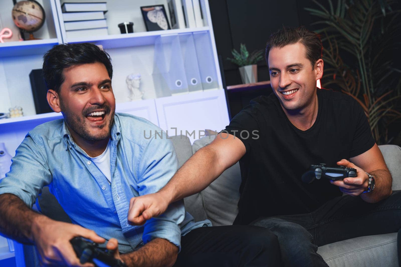 Winner and loser players of buddy friend gamers playing video game on TV using joysticks in studio room with neon blue light. Comfy living indoor at home place with cheerful fighting winner. Sellable.