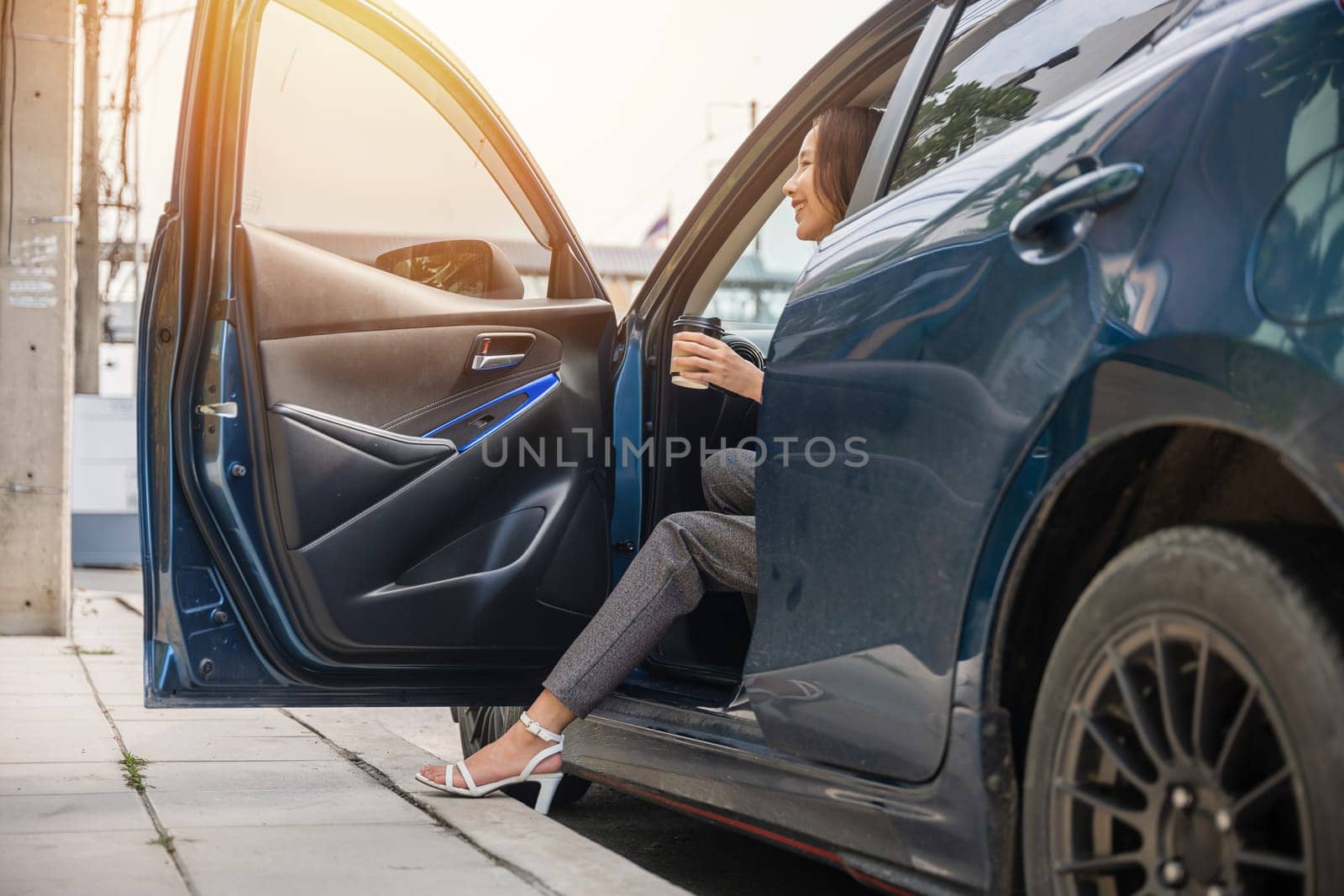 Businesswoman in sleek suit is sitting in modern car. Her long slim leg in high heel shoe opens door exuding elegance and sensuality. Getting out of luxury vehicle is symbol of her glamour and success