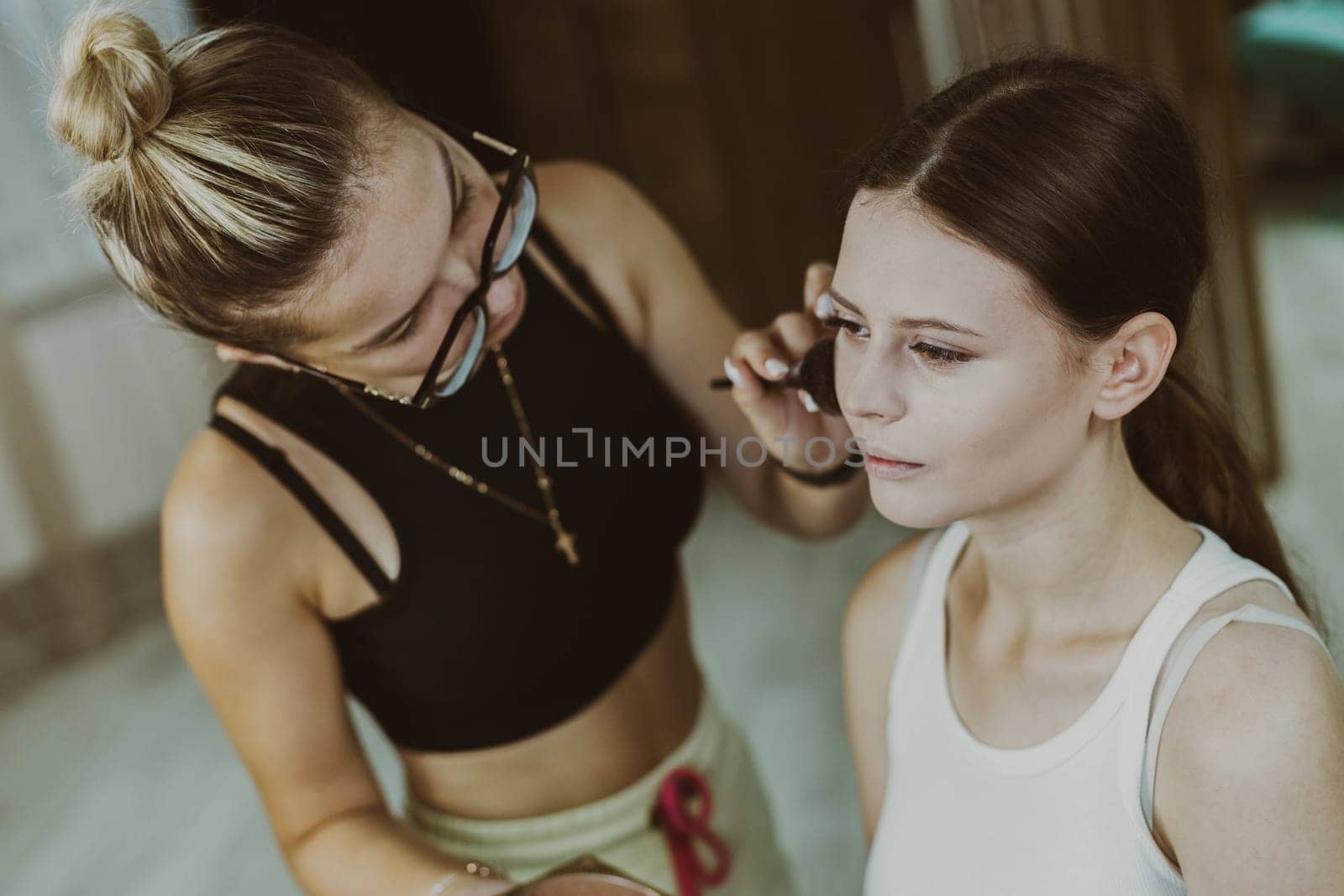 A young makeup artist applies powder with a brush to a girl s cheekbones. by Nataliya