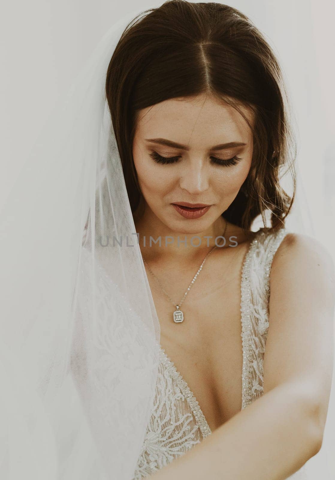 Portrait of one beautiful young Caucasian brunette bride in a white dress with a veil on her head looking down sweetly, side view, close-up.