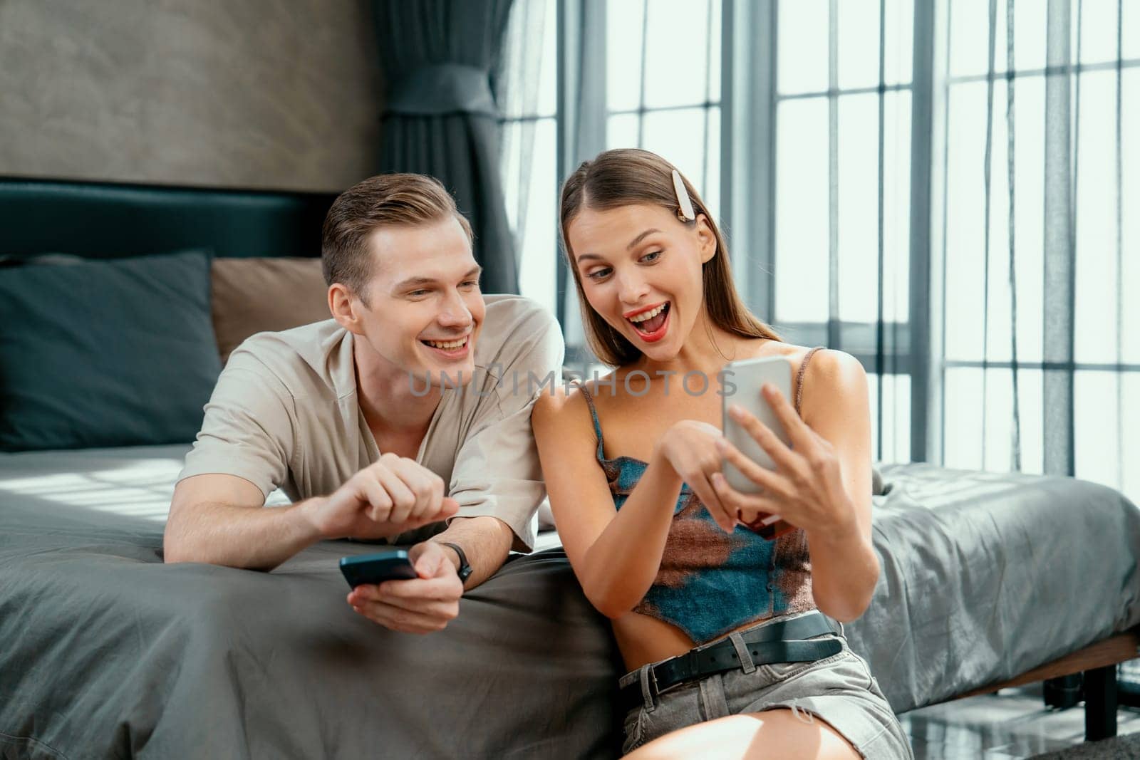 Young couple sit in the home bedroom using online payment app and digital wallet on smartphone to pay with credit card. E commerce shopping and modern purchasing via mobile internet. Unveiling