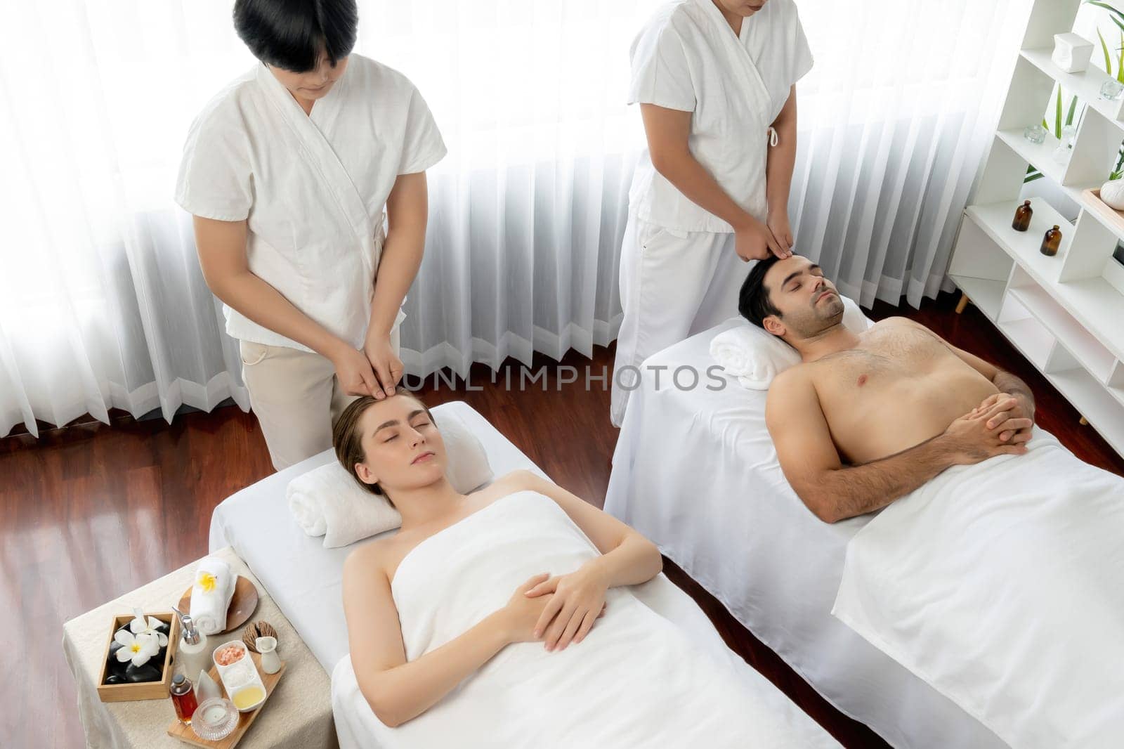 Caucasian couple enjoying relaxing anti-stress head massage and pampering facial beauty skin recreation leisure in dayspa modern light ambient at luxury resort or hotel spa salon. Quiescent
