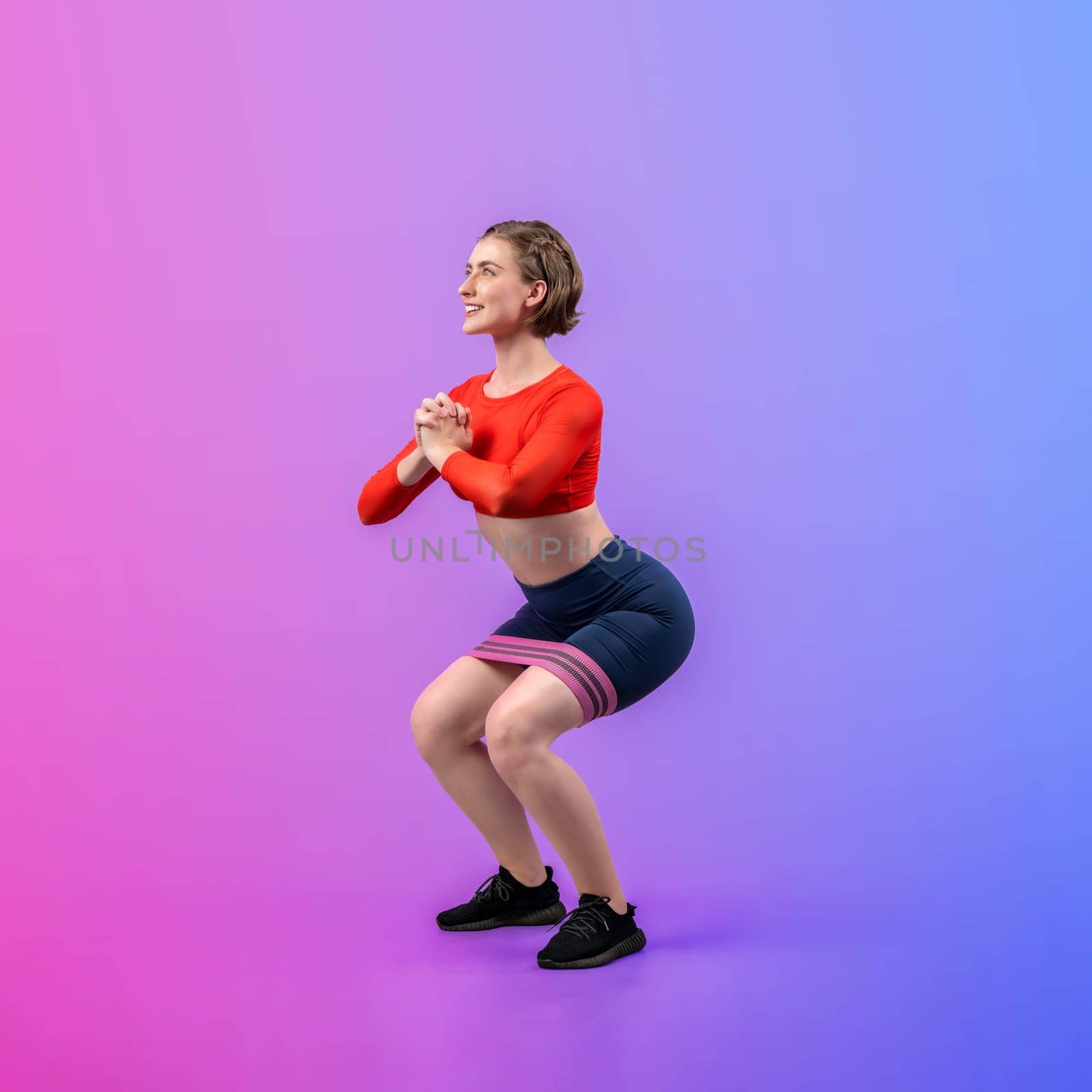 Full body length gaiety shot athletic and sporty young woman with fitness elastic resistance band in squat exercise posture on isolated background. Healthy active and body care lifestyle.