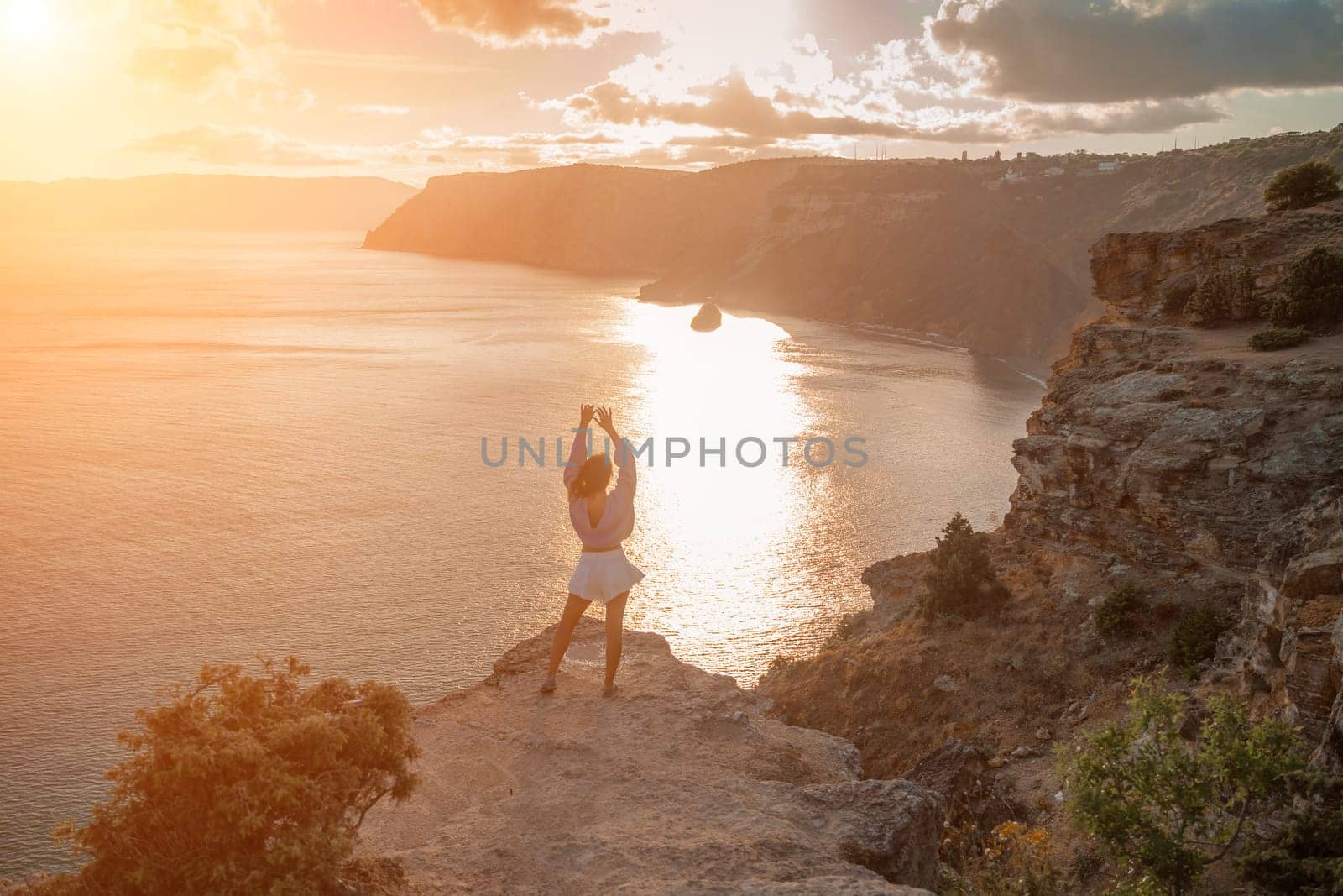 Free girl with open arms at sunset over the sea, sun over clouds, sunset in the mountains, golden hour, silhouette of a woman at sunset on the mountain.