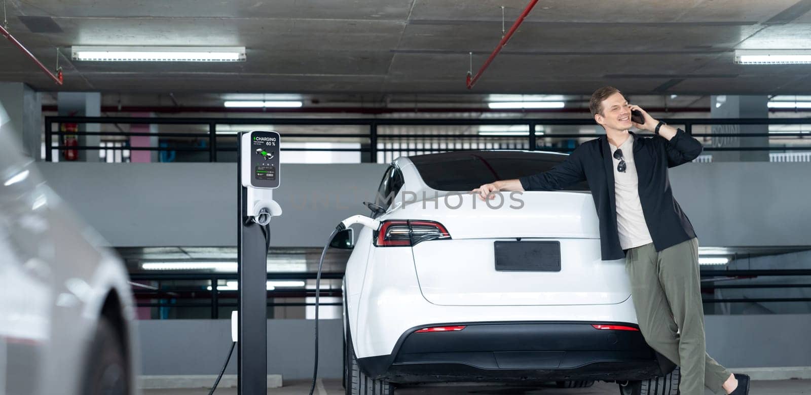 Young man travel with EV electric car to shopping center parking lot charging in downtown city showing urban sustainability lifestyle by green clean rechargeable energy of electric vehicle innards