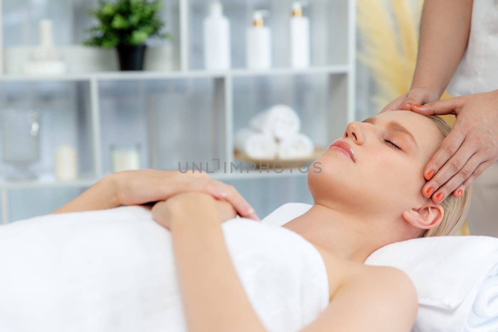 Caucasian woman enjoying relaxing anti-stress head massage and pampering facial beauty skin recreation leisure in dayspa modern light ambient at luxury resort or hotel spa salon. Quiescent