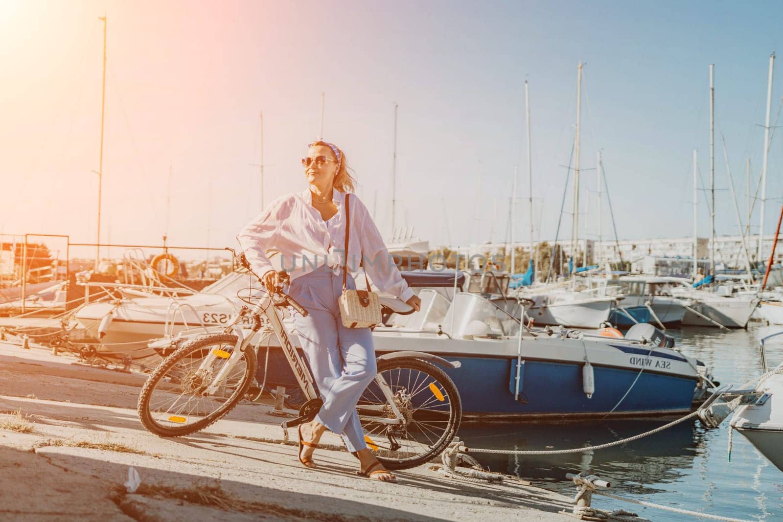 Woman enjoys bike ride along waterfront, Marina surroundings. She is wearing a white shirt and blue jeans, and she has a handbag with her. Capturing outdoor bike ride by waterfront. by Matiunina