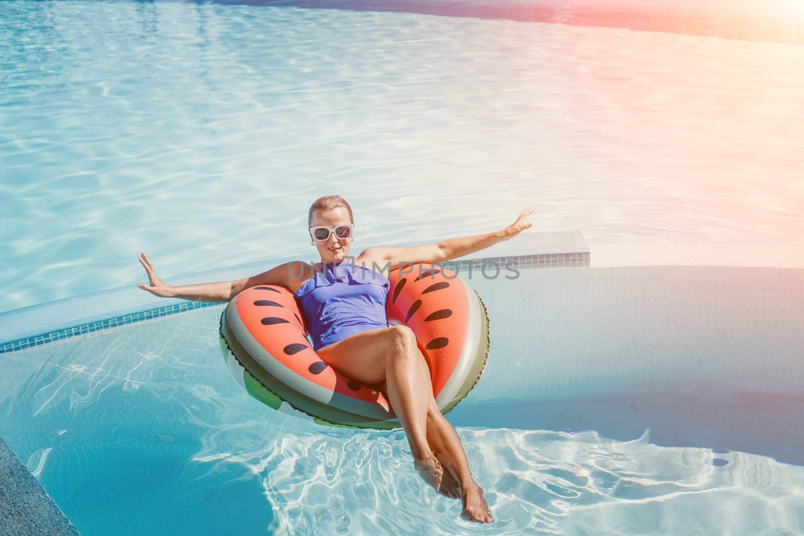 Happy woman in a swimsuit and sunglasses floating on an inflatable ring in the form of a watermelon, in the pool during summer holidays and vacations. Summer concept. by Matiunina