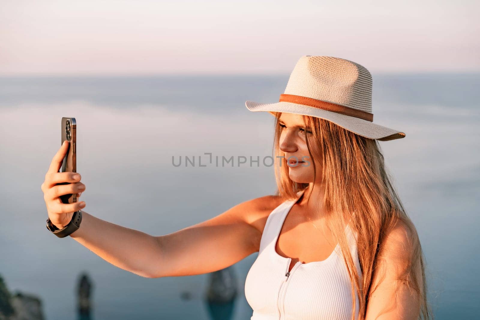 Selfie woman in hat, white tank top and shorts makes selfie shot mobile phone post photo social network outdoors on sea background beach people vacation lifestyle travel concept. by Matiunina