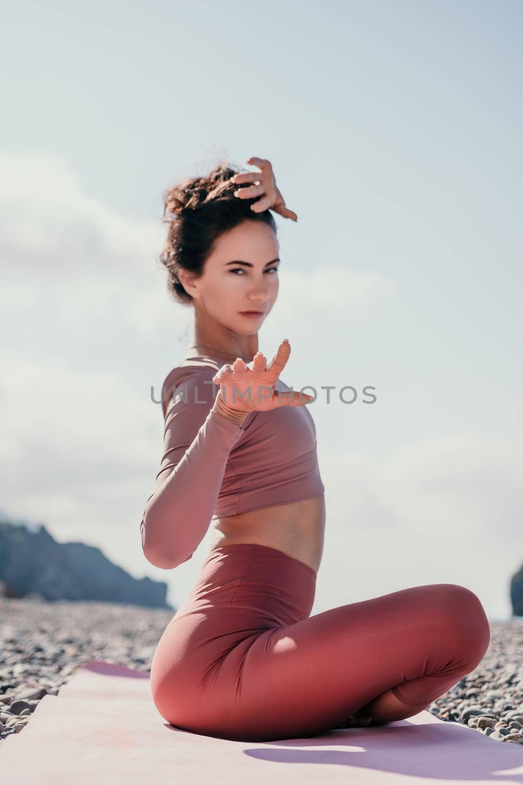 Middle aged well looking woman with black hair, fitness instructor in leggings and tops doing stretching and pilates on yoga mat near the sea. Female fitness yoga routine concept. Healthy lifestyle by panophotograph