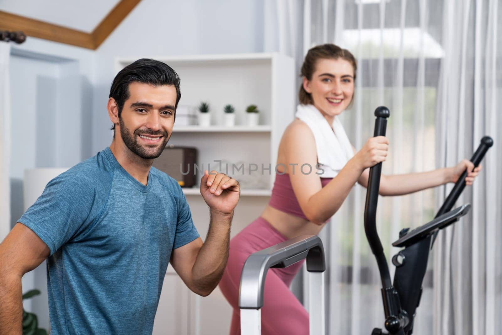 Athletic and sporty couple running on elliptical running machine at gaiety home. by biancoblue