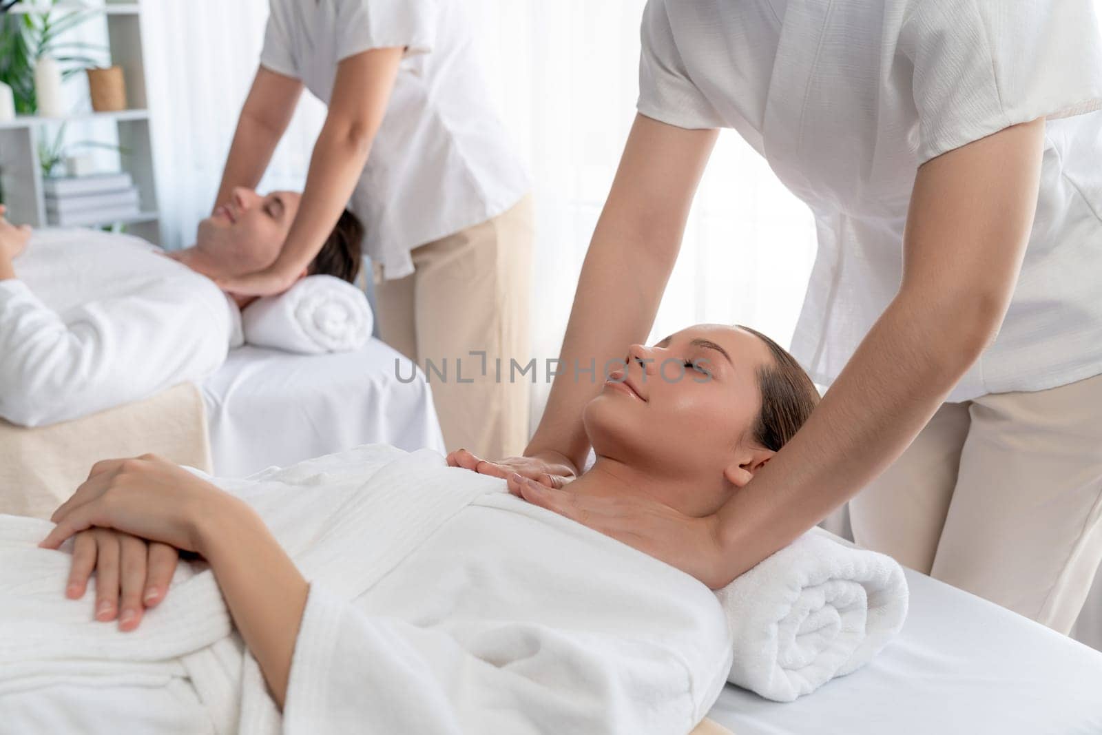Caucasian couple customer enjoying relaxing anti-stress spa massage and pampering with beauty skin recreation leisure in day light ambient salon spa at luxury resort or hotel. Quiescent