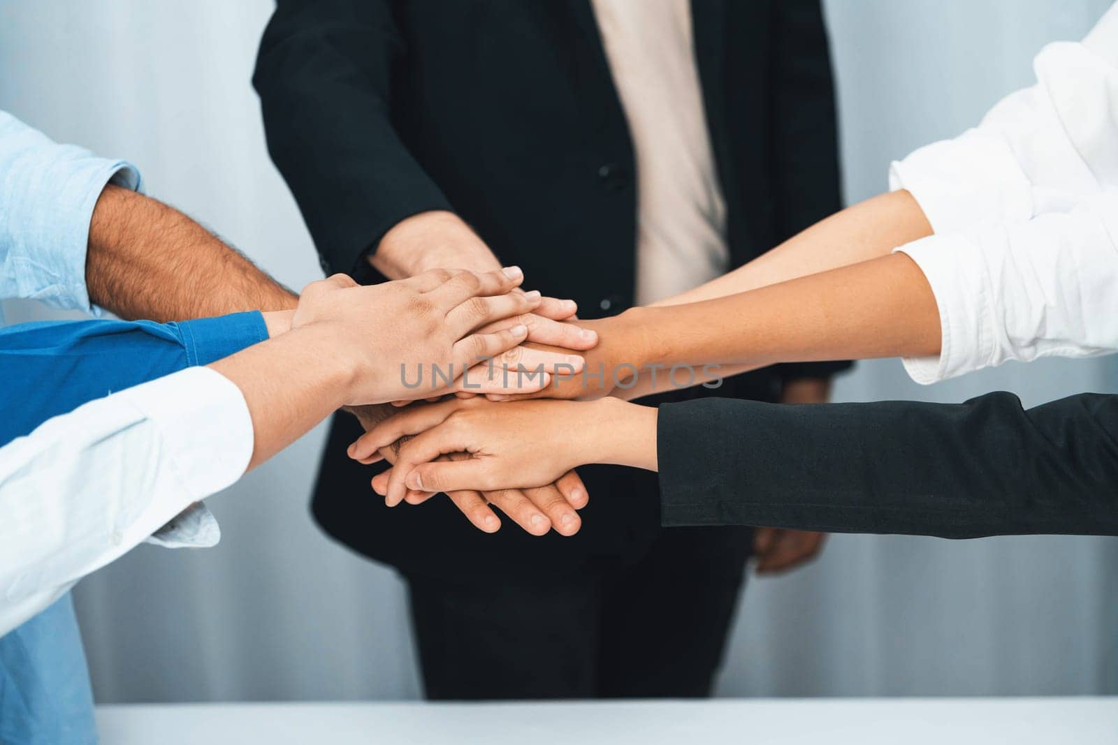 Group of diverse office worker join hand together in office room symbolize business synergy and strong productive teamwork in workplace. Cooperation and unity between business employee. Prudent