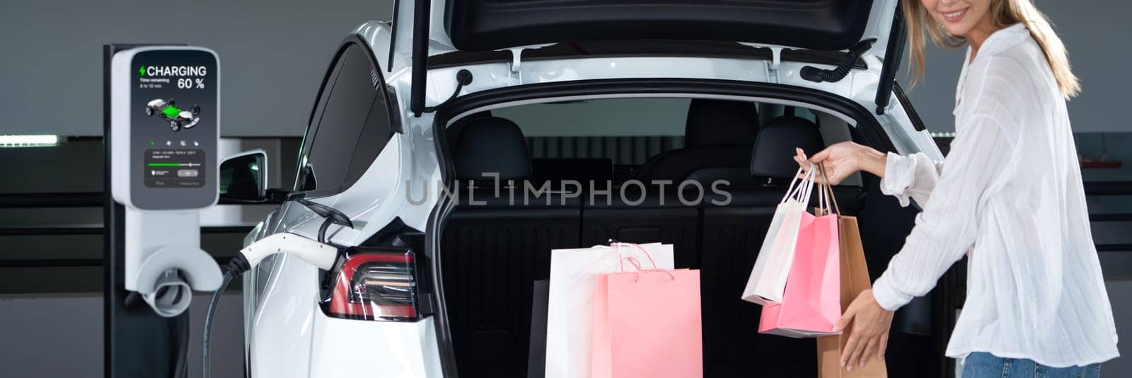 Young woman travel with EV electric car to shopping center parking lot innards by biancoblue