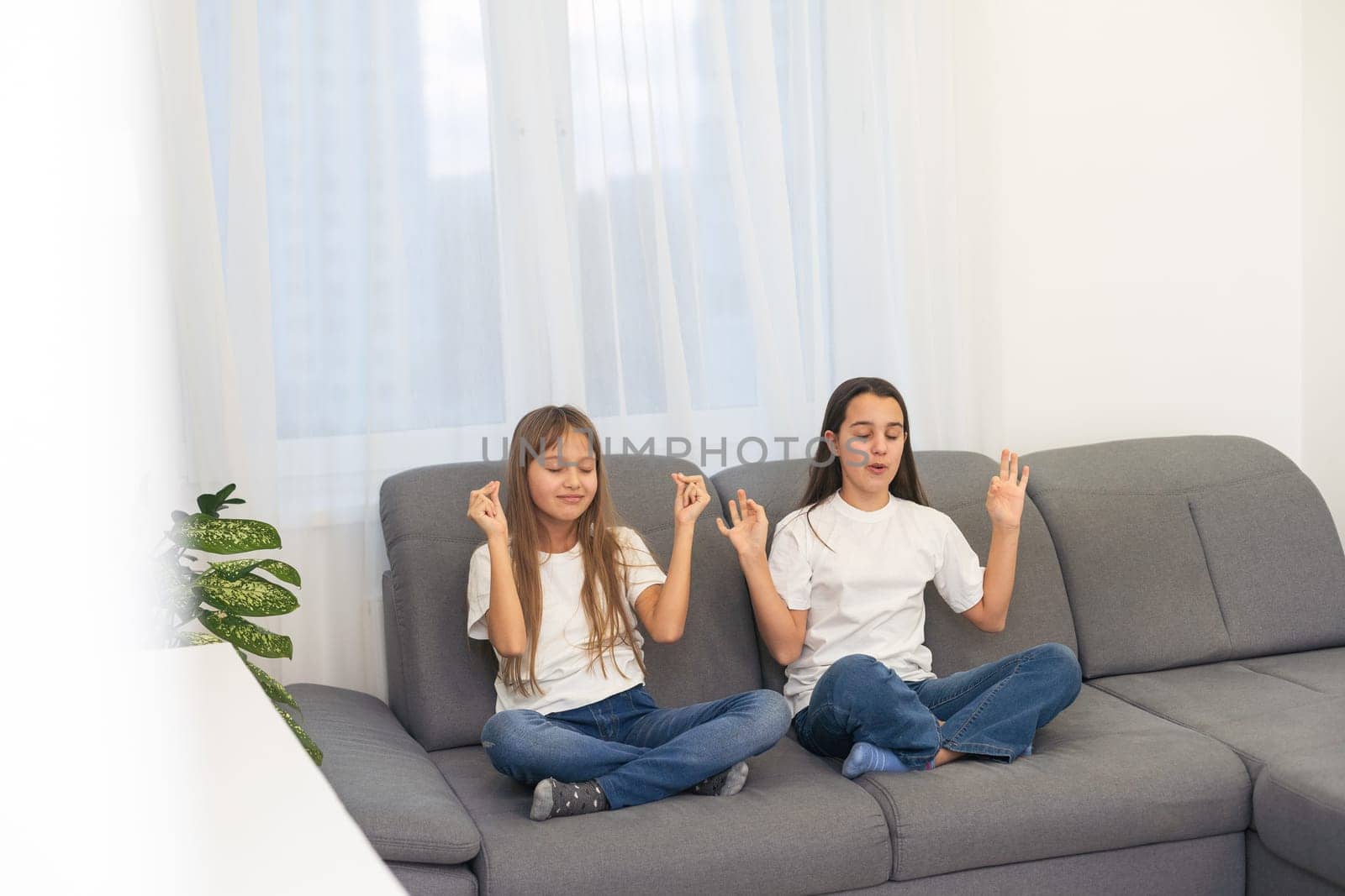 People, relationships, family, relaxation, yoga and meditation concept. girls sitting on bed, looking up, making mudra gesture, praying or meditating by Andelov13
