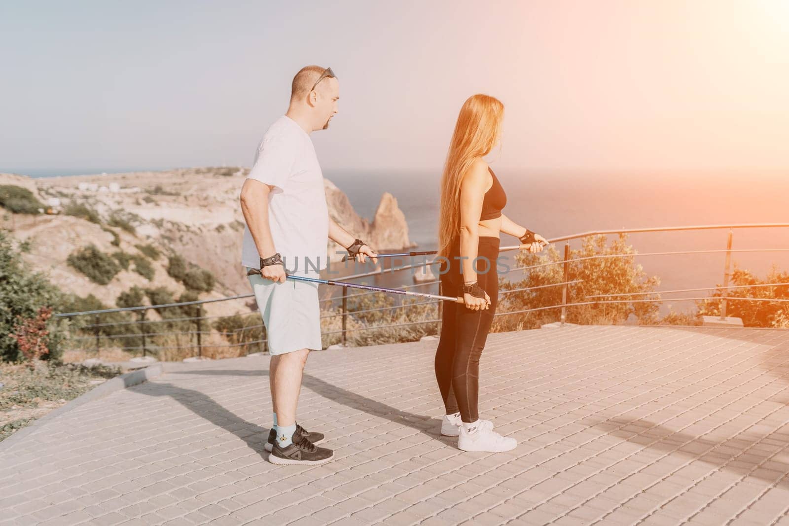 Happy Middle aged couple or friends practicing nordic walking in park near sea. Mature couple with trekking poles walking, practicing Nordic walking outdoors. Aging youthfully and sport concept.