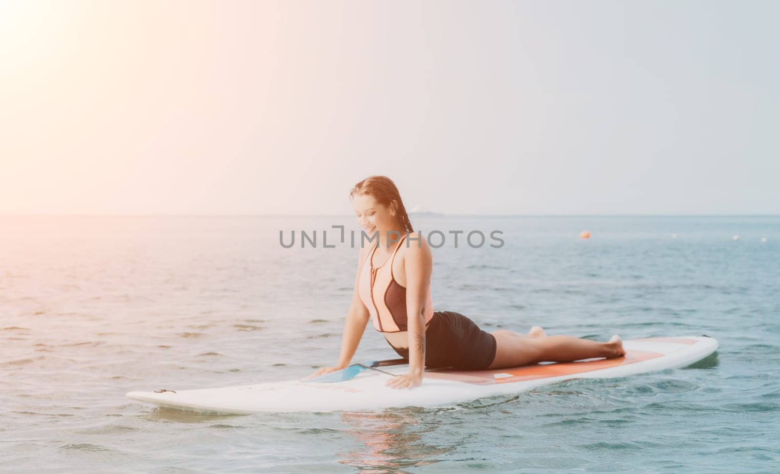 Woman sup yoga. Happy young sporty woman practising yoga pilates on paddle sup surfboard. Female stretching doing workout on sea water. Modern individual female outdoor summer sport activity