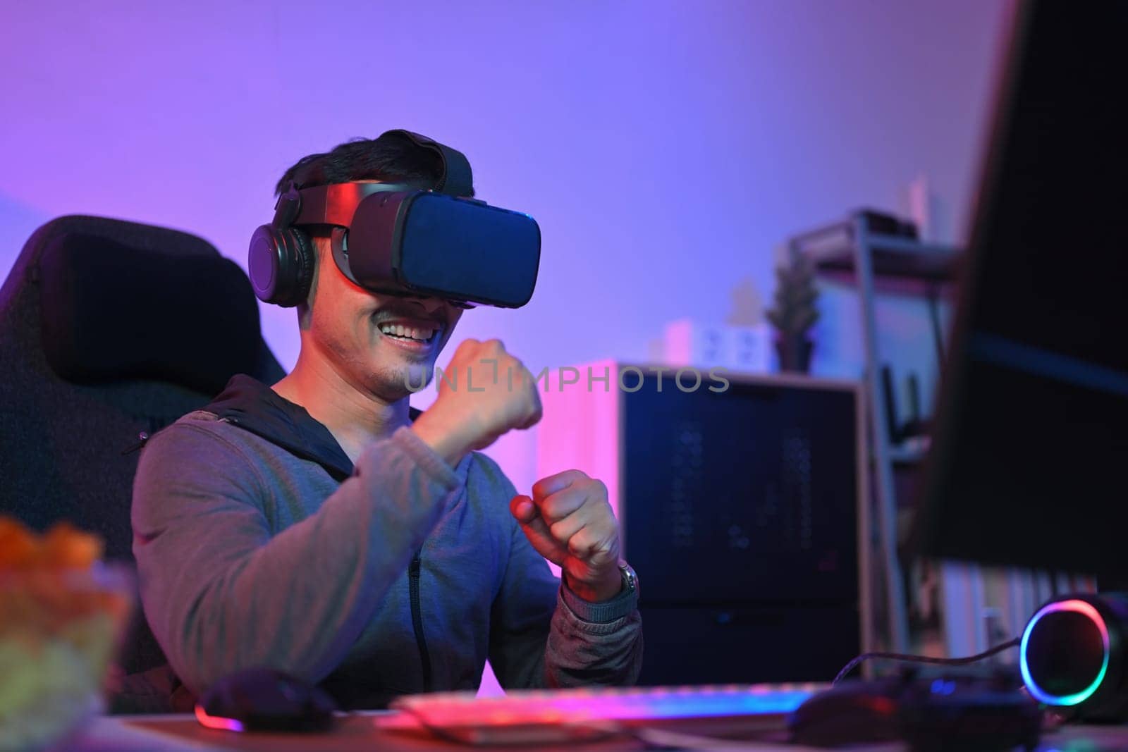 Happy excited man playing boxing game in VR glasses at home with neon led lights.