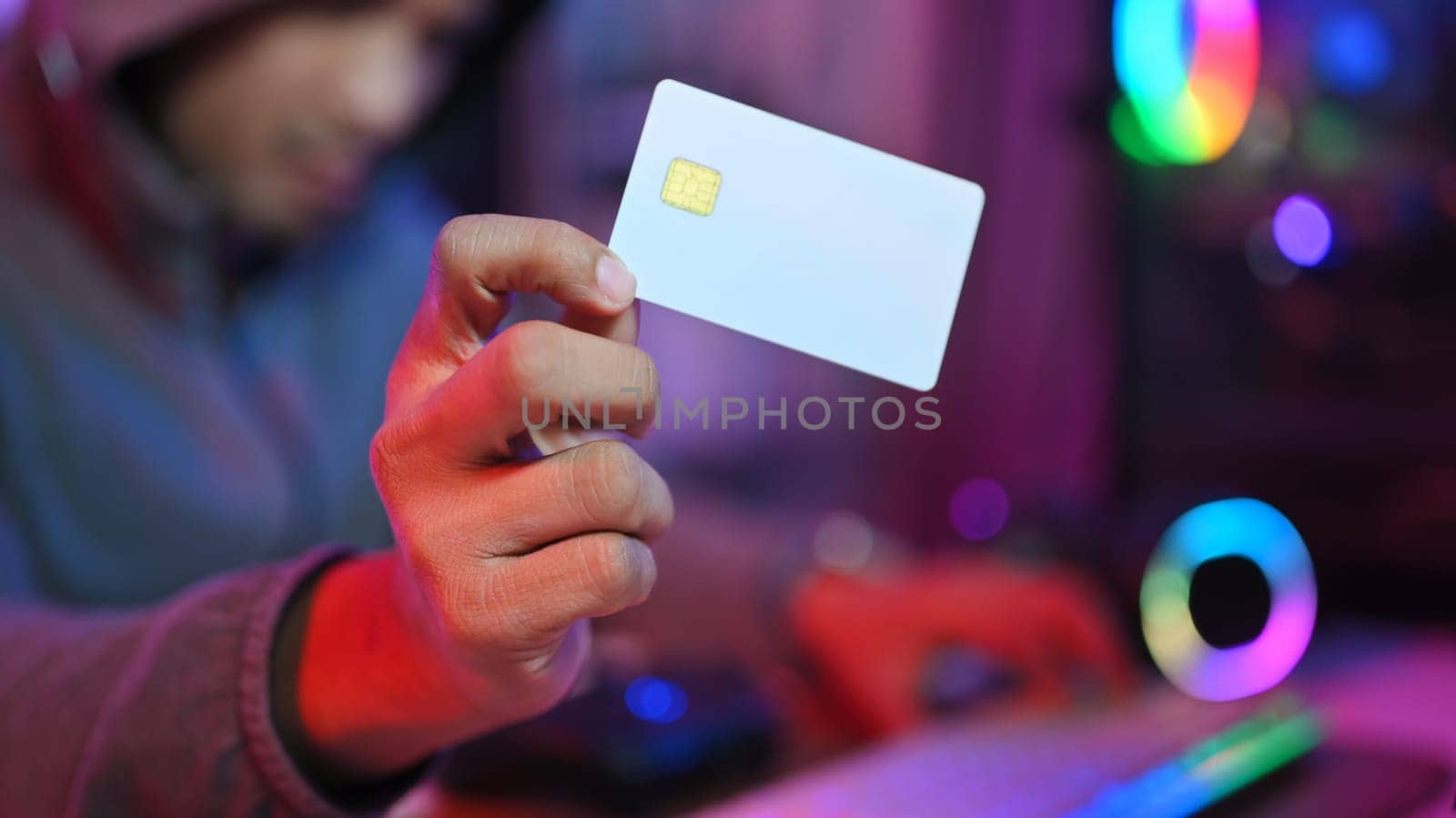 Anonymous hacker in hoodie holding credit card in his hand. Network security and cyber crime concept.