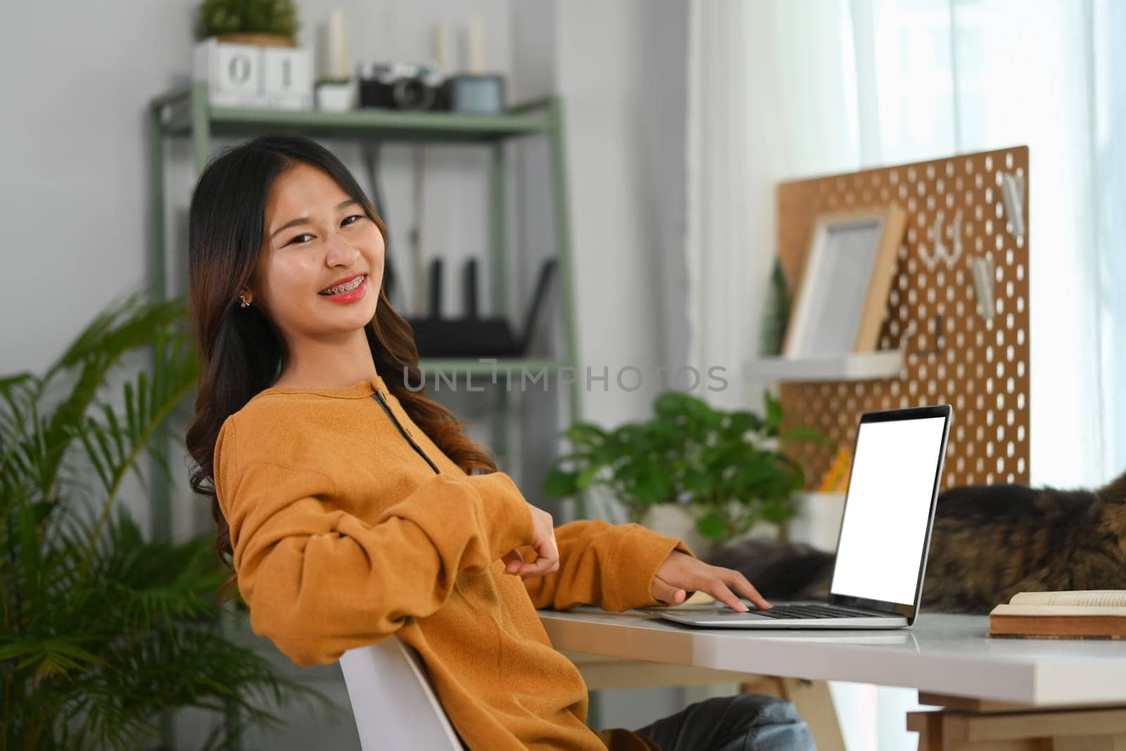 Portrait of cheerful young female freelancer working on laptop at home by prathanchorruangsak