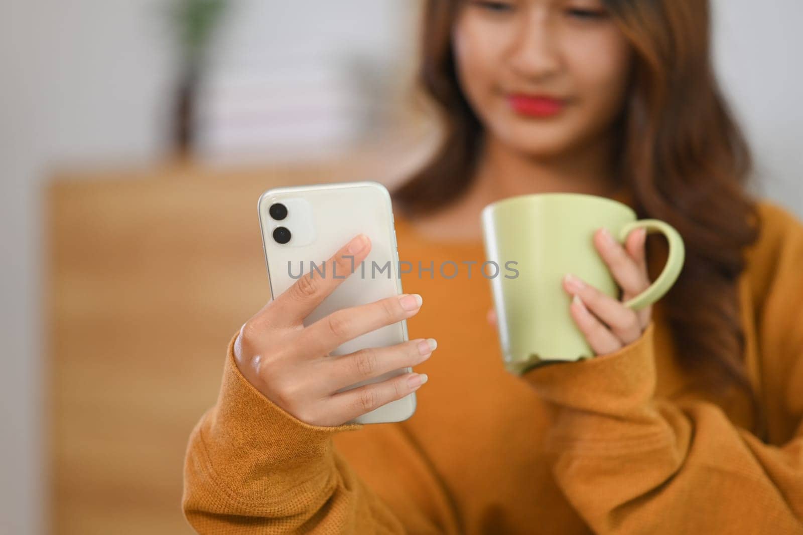 Happy young woman drinking tea and checking social media on smart phone.