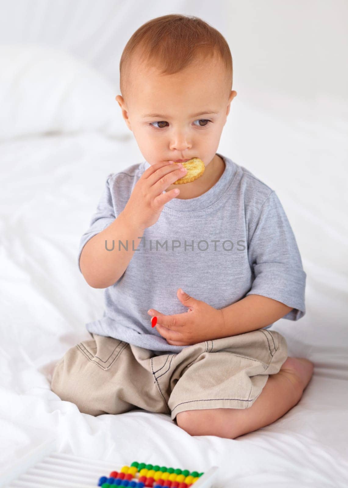 Cute, bed and baby eating biscuit for yummy snack playing with abacus for education. Child development, sweet and hungry young boy kid, infant or toddler enjoying a cracker in bedroom at home. by YuriArcurs