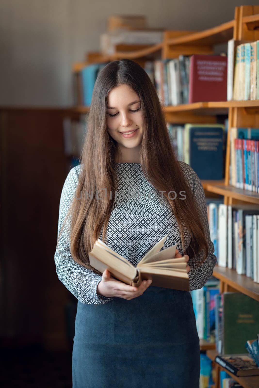 Cheerful high school female student reading book in library by VitaliiPetrushenko