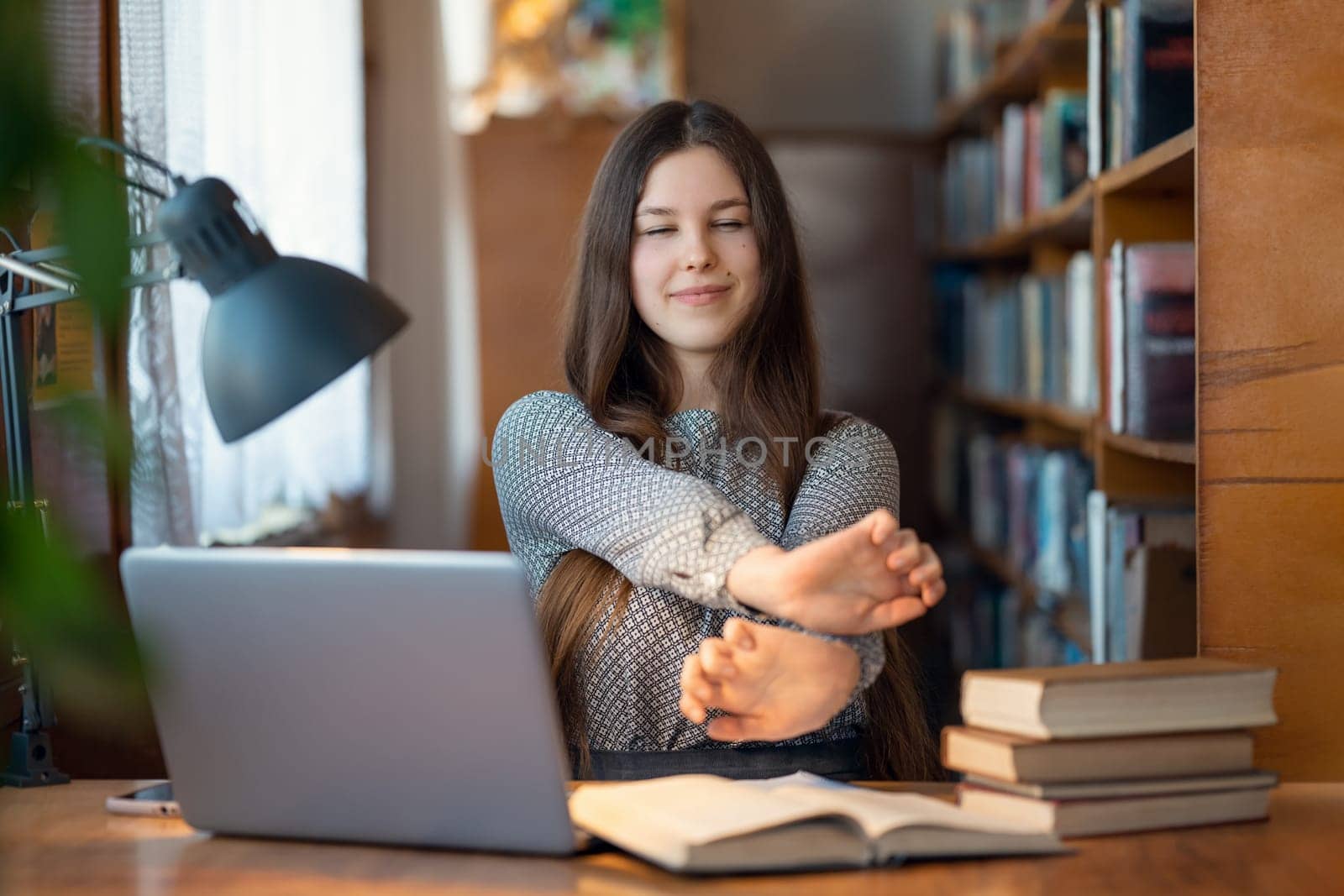 Young brunette girl sitting at a table in the library and doing some stretching for her hands by VitaliiPetrushenko