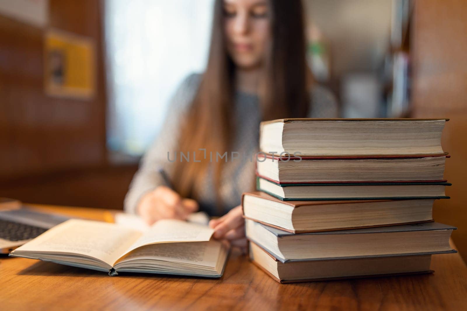 Concentrated young brunette student girl writing in the notebook and working with book on the background