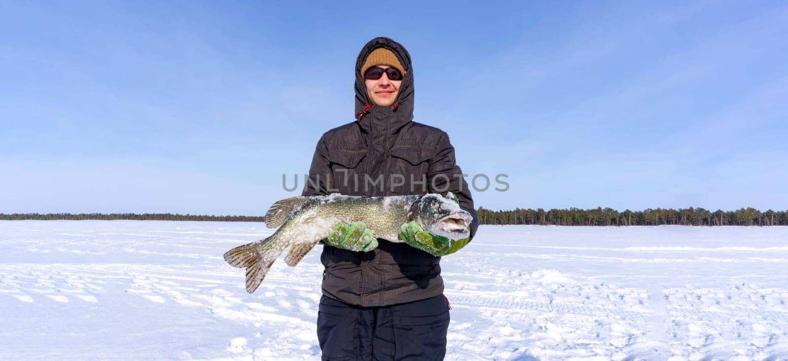 Man Holding a Fish pike in the Snow. Winter fishing, adventure. Banner, copy space