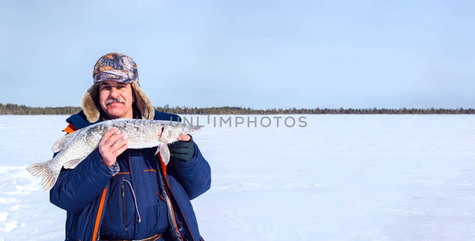 Winter fishing. Man Holding a Fish pike in Hands. Banner, copy space