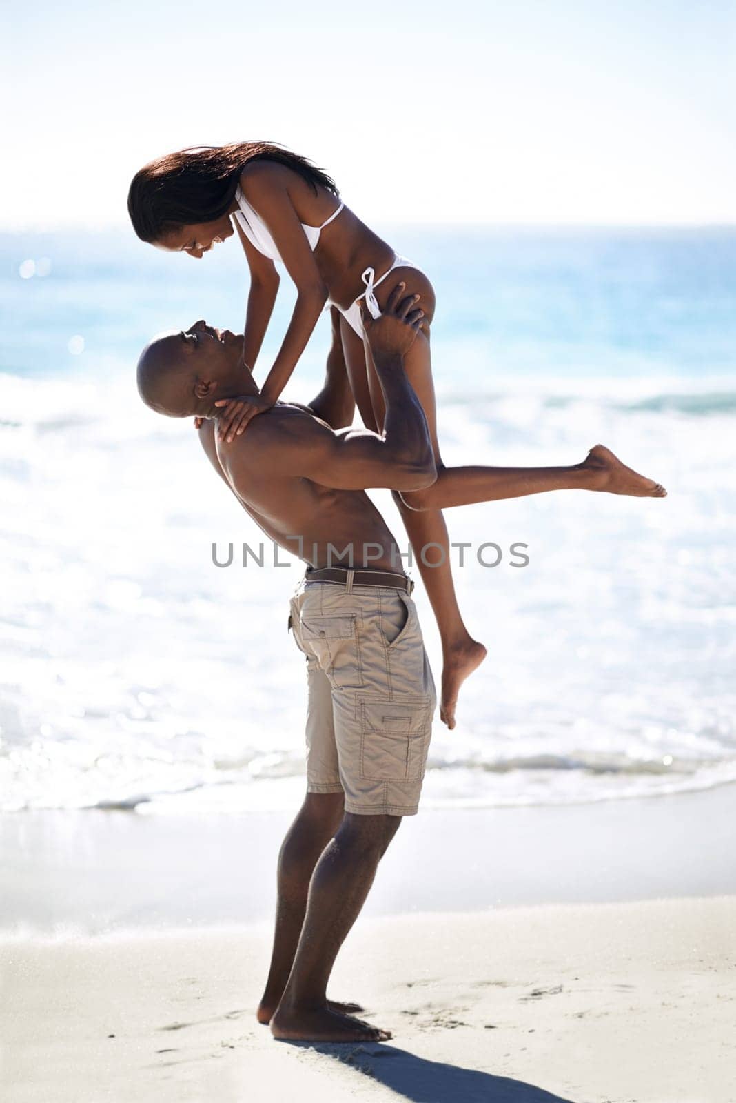 Lifting, hug and couple at a beach with love, romance and bonding in nature together. Support, travel and black people embrace at sea with freedom, energy and excited for summer, vacation or trip.