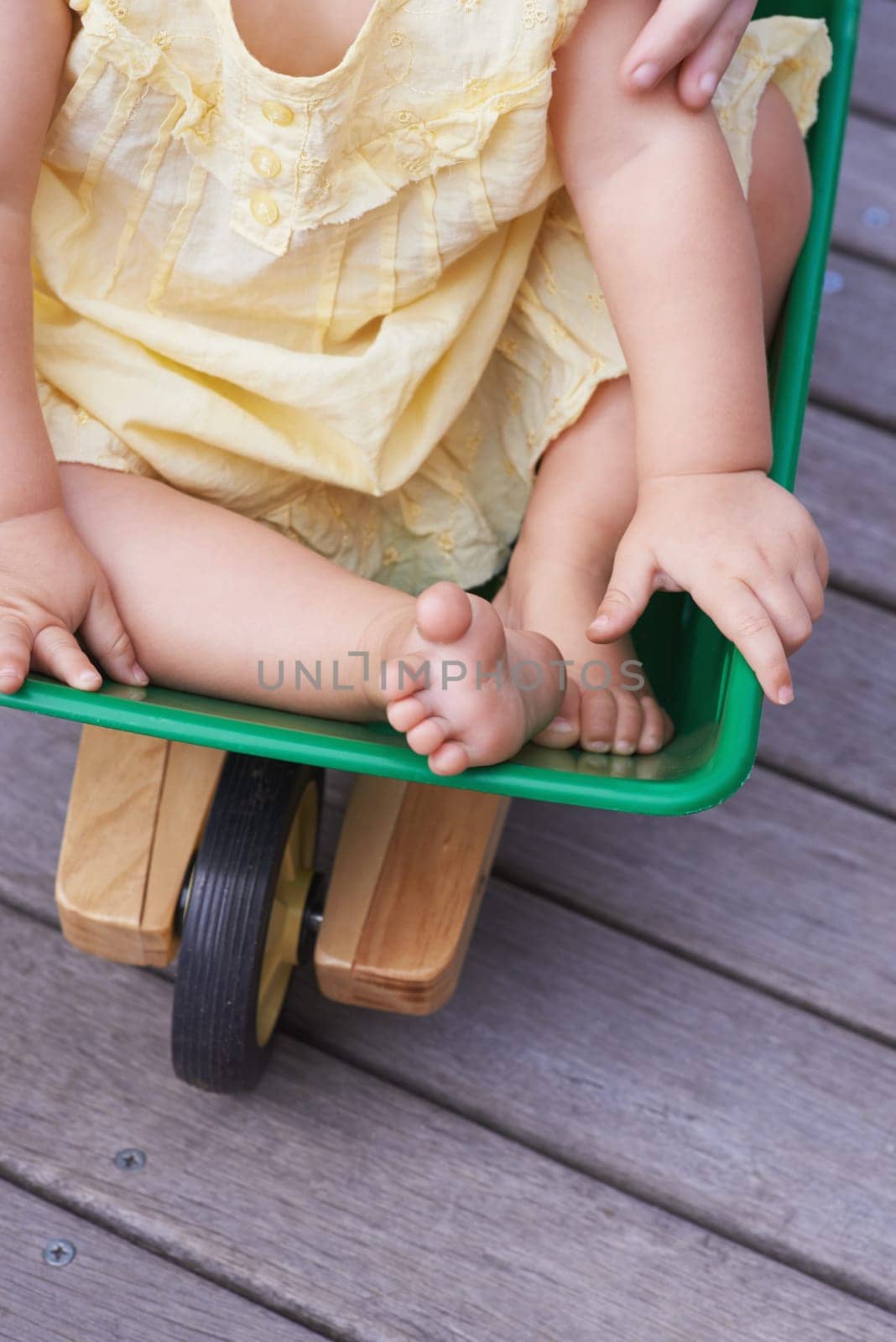 Baby, child and riding toy wagon in outdoors, plastic and fun activity for childhood. Kid, toddler and wheelbarrow for playing games on porch or deck, closeup and relaxing in construction equipment by YuriArcurs