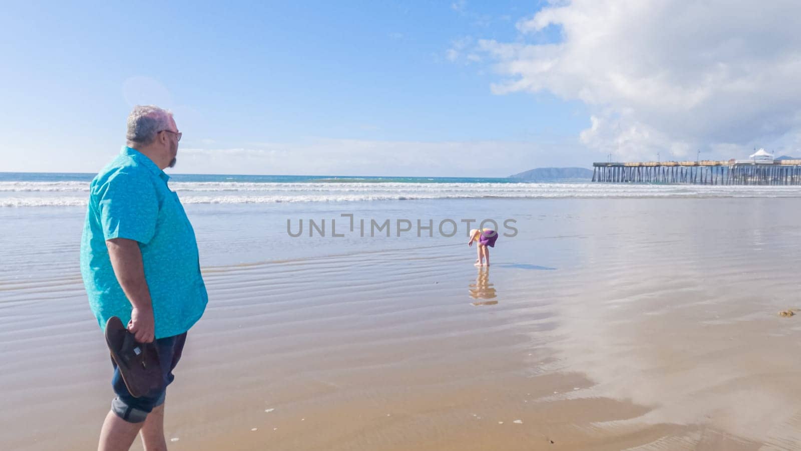 Father and daughter enjoy a leisurely winter walk along the picturesque Pismo Beach, sharing quality time together amid the serene backdrop of gently crashing waves.