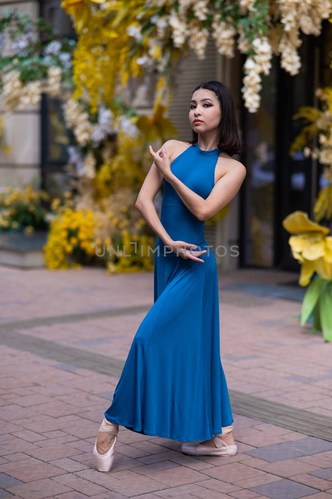 Beautiful Asian ballerina posing against the backdrop of a building decorated with flowers