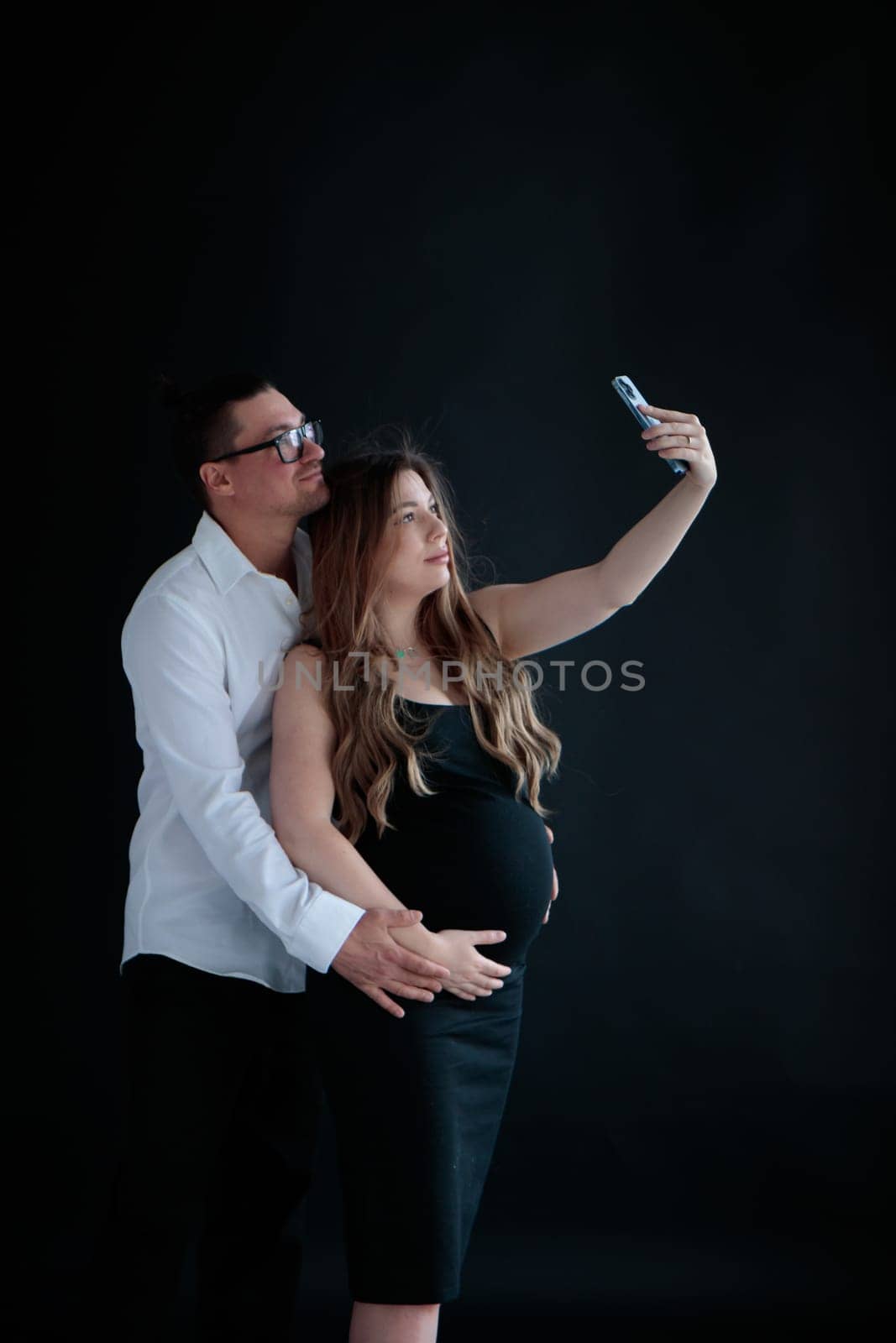 A young couple of parents-to-be taking selfies against at a black background