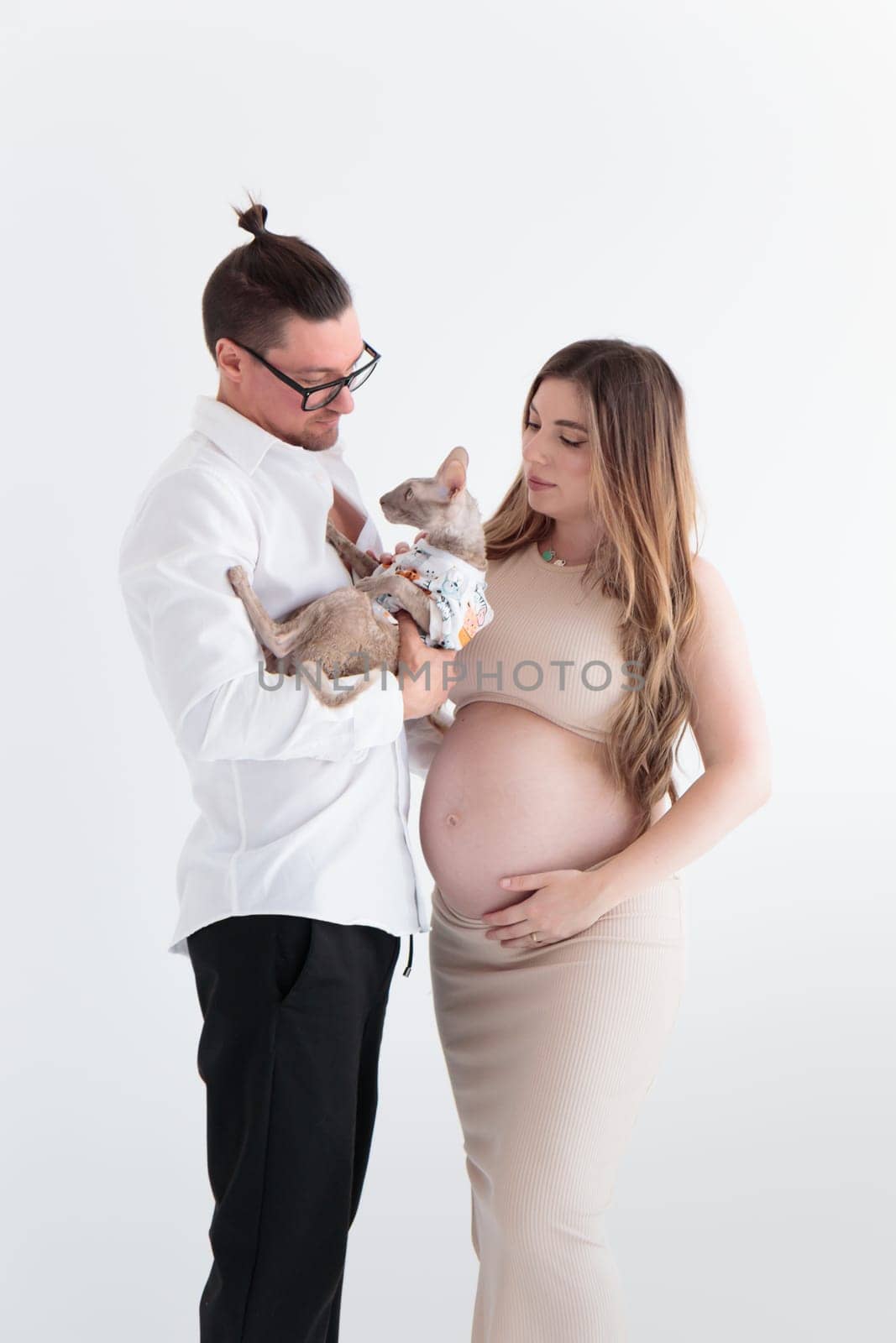 A young couple of expectant parents hold a cat in the arms