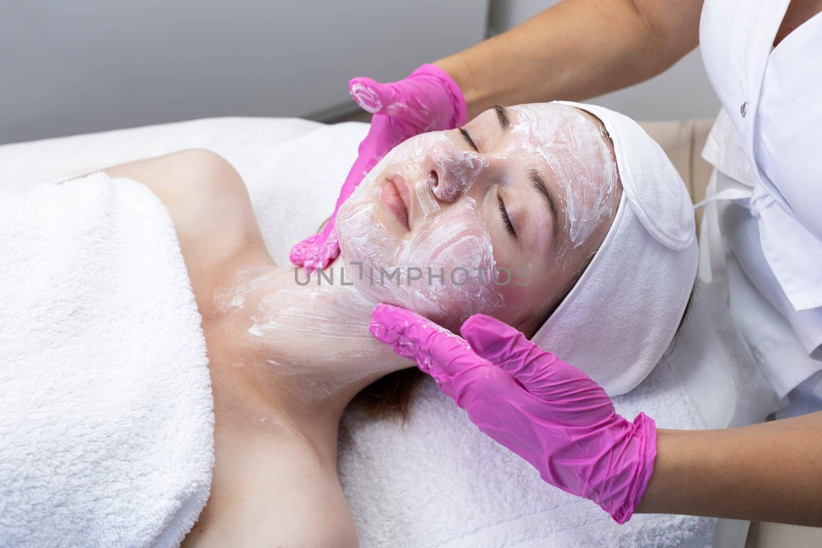 Cosmetologist applies moisturizing cream on female pretty face for rejuvenation face skin, rehydration cosmetic procedure in spa. Professional beautician applying revitalizing cream mask, skincare