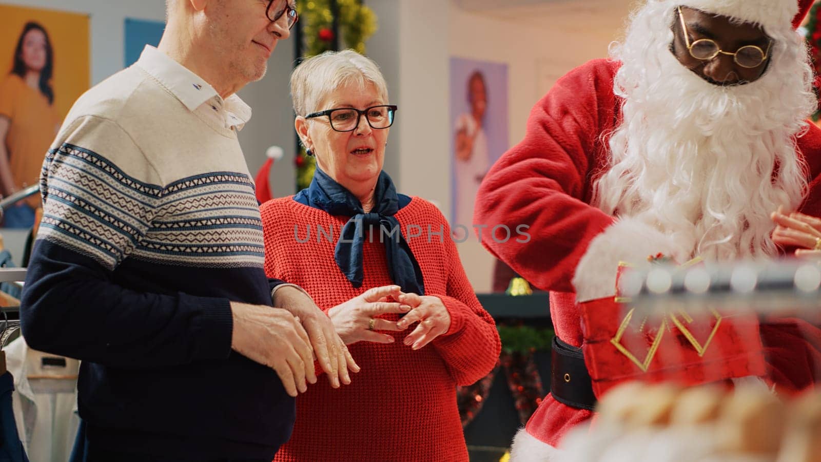 Clients participating in Christmas raffle hold by retail assistant dressed as Santa Claus in festive ornate clothing store. Lucky elderly couple excited after winning promotional fashion shop contest