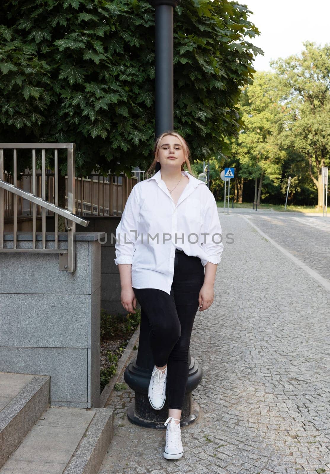 Portrait Pretty Plus Size 20s Woman, Gentle Zoomer Outdoor Leans to Street Light. Young Relaxed Caucasian Girl Of Gen Z. Vertical Plane.