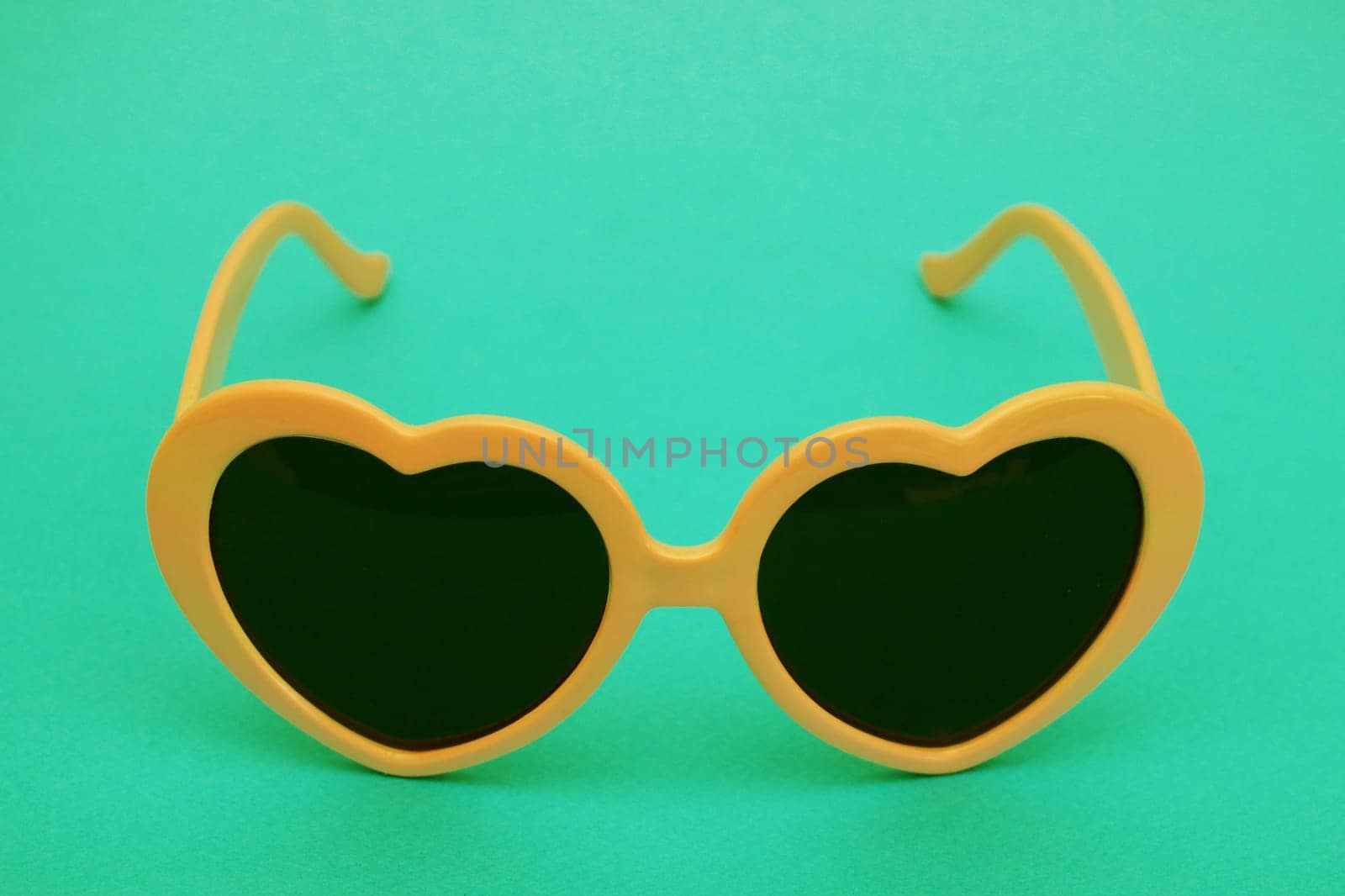 Dark opaque glasses with an orange plastic frame on a green background.