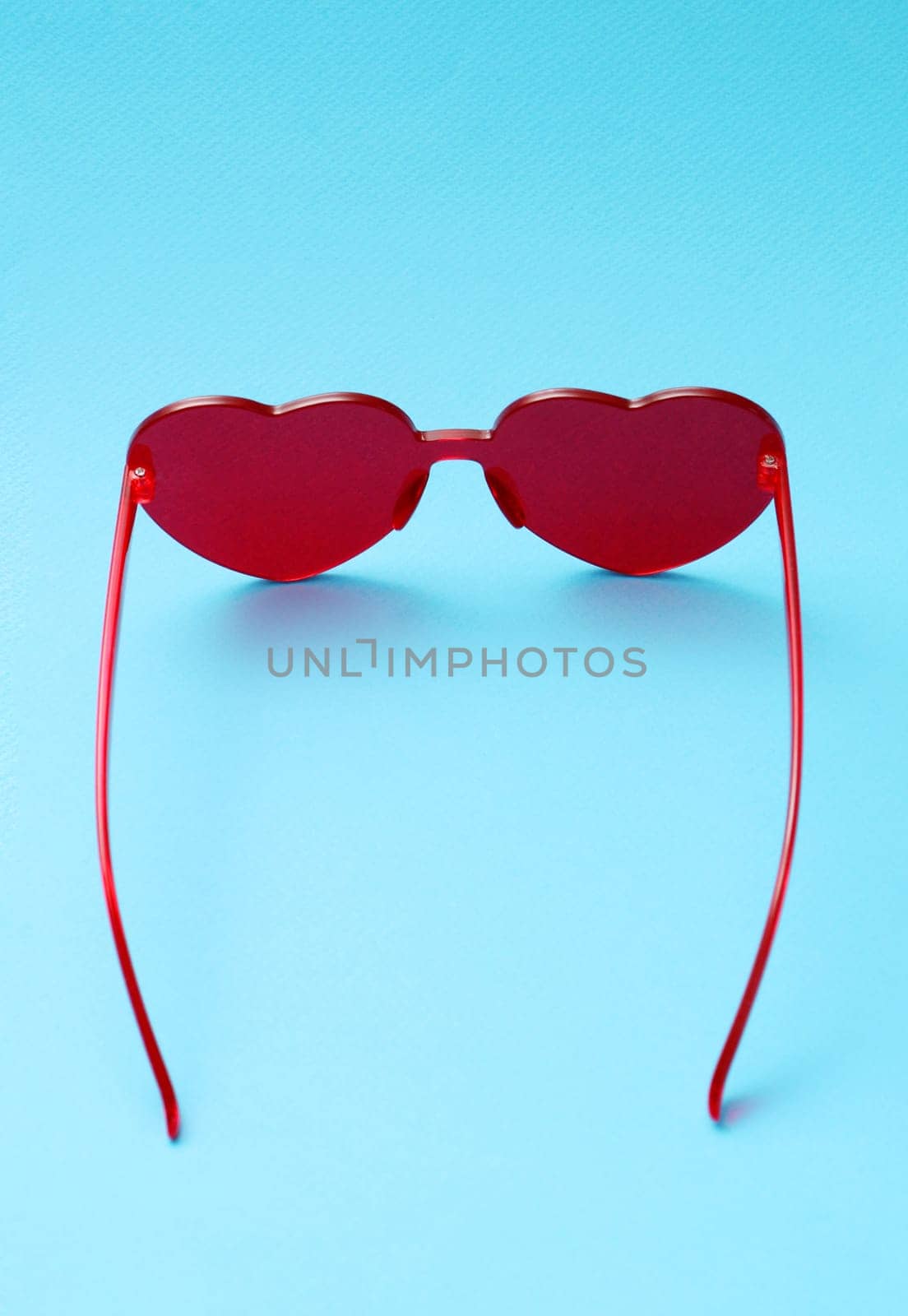 Vertical photo of red sunglasses on a blue background top view.