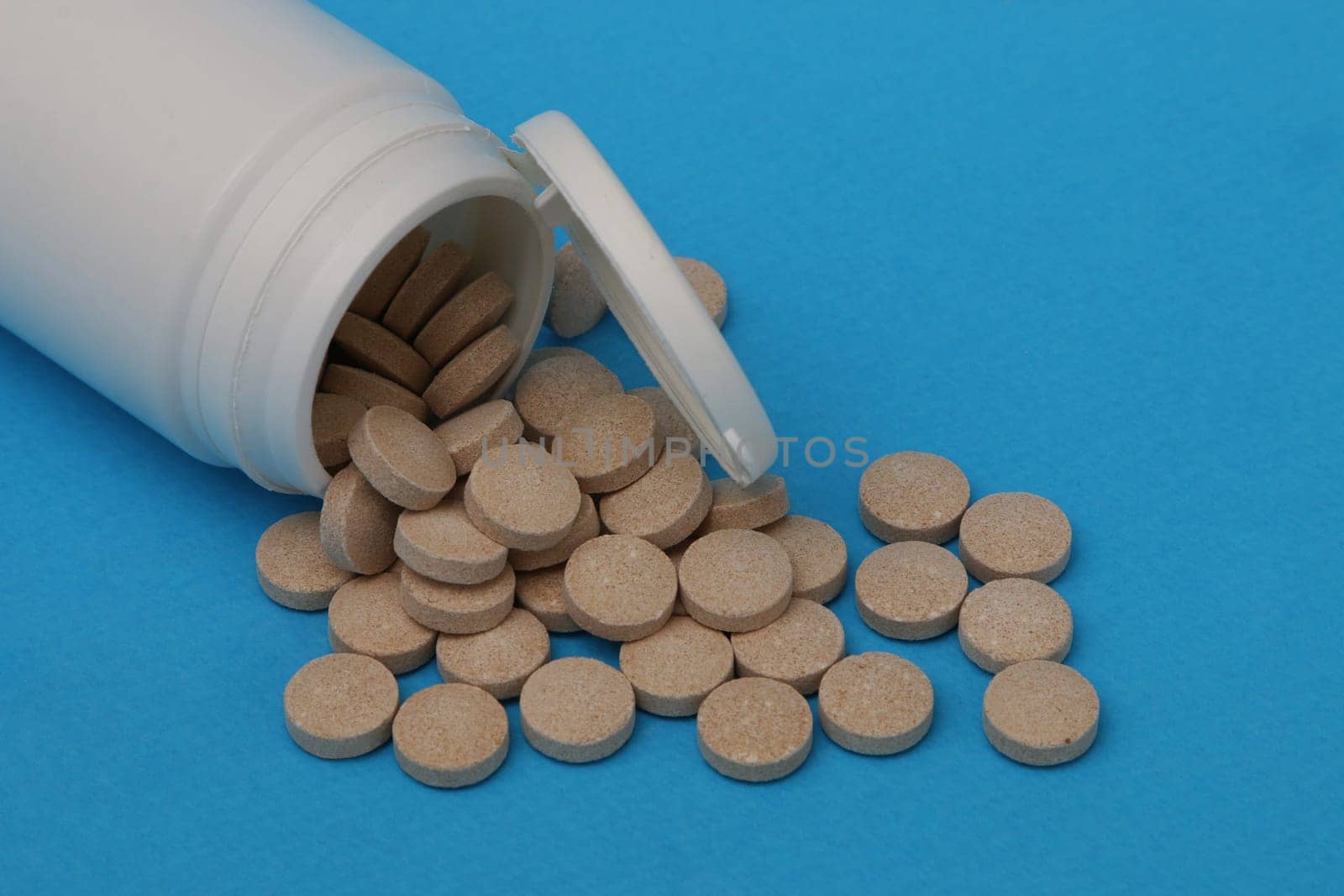 White plastic bottle with scattered brown pills on a blue paper background. Medicine and health concept.