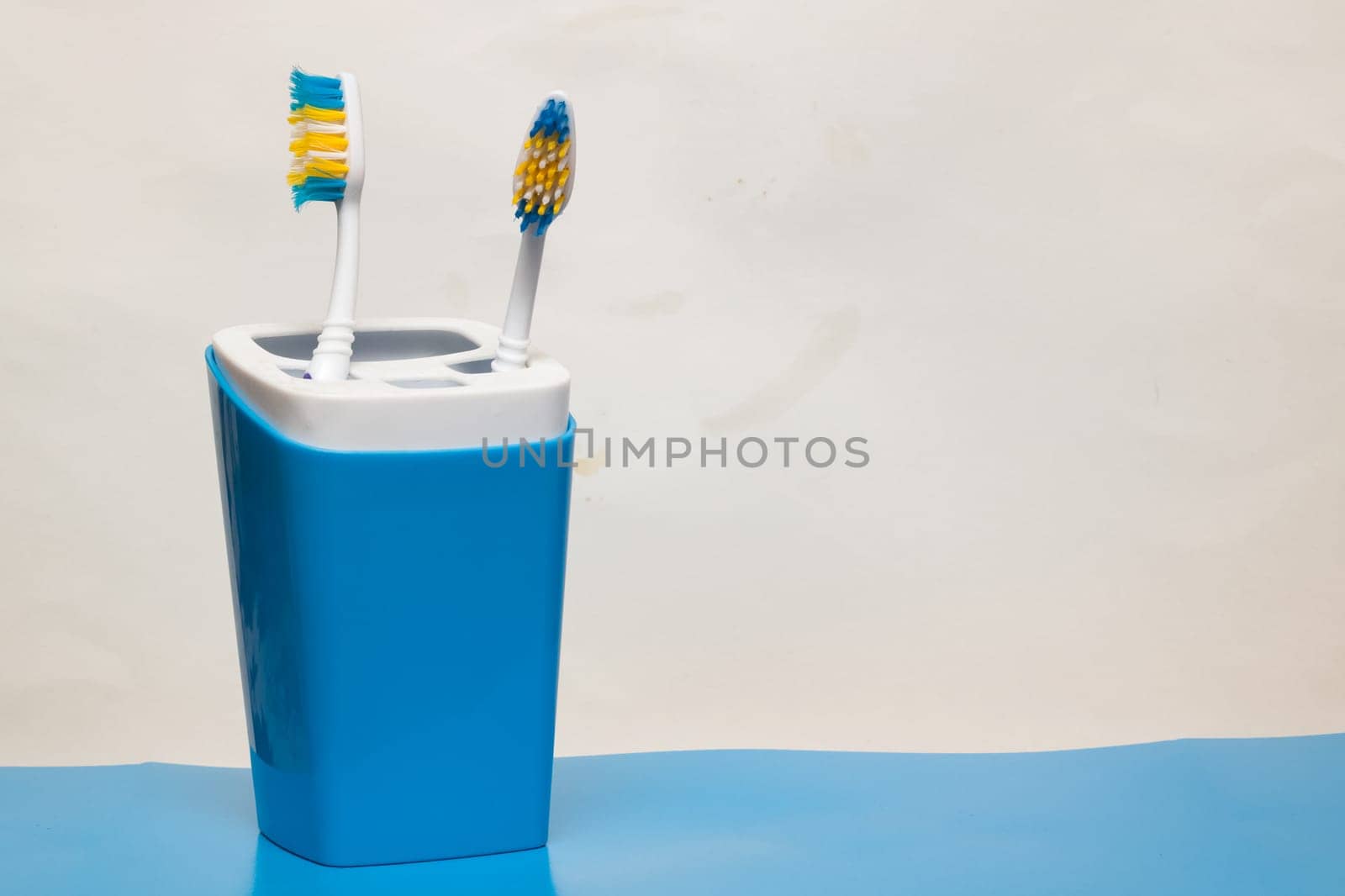 Two toothbrushes in a glass on a blue background, copy space