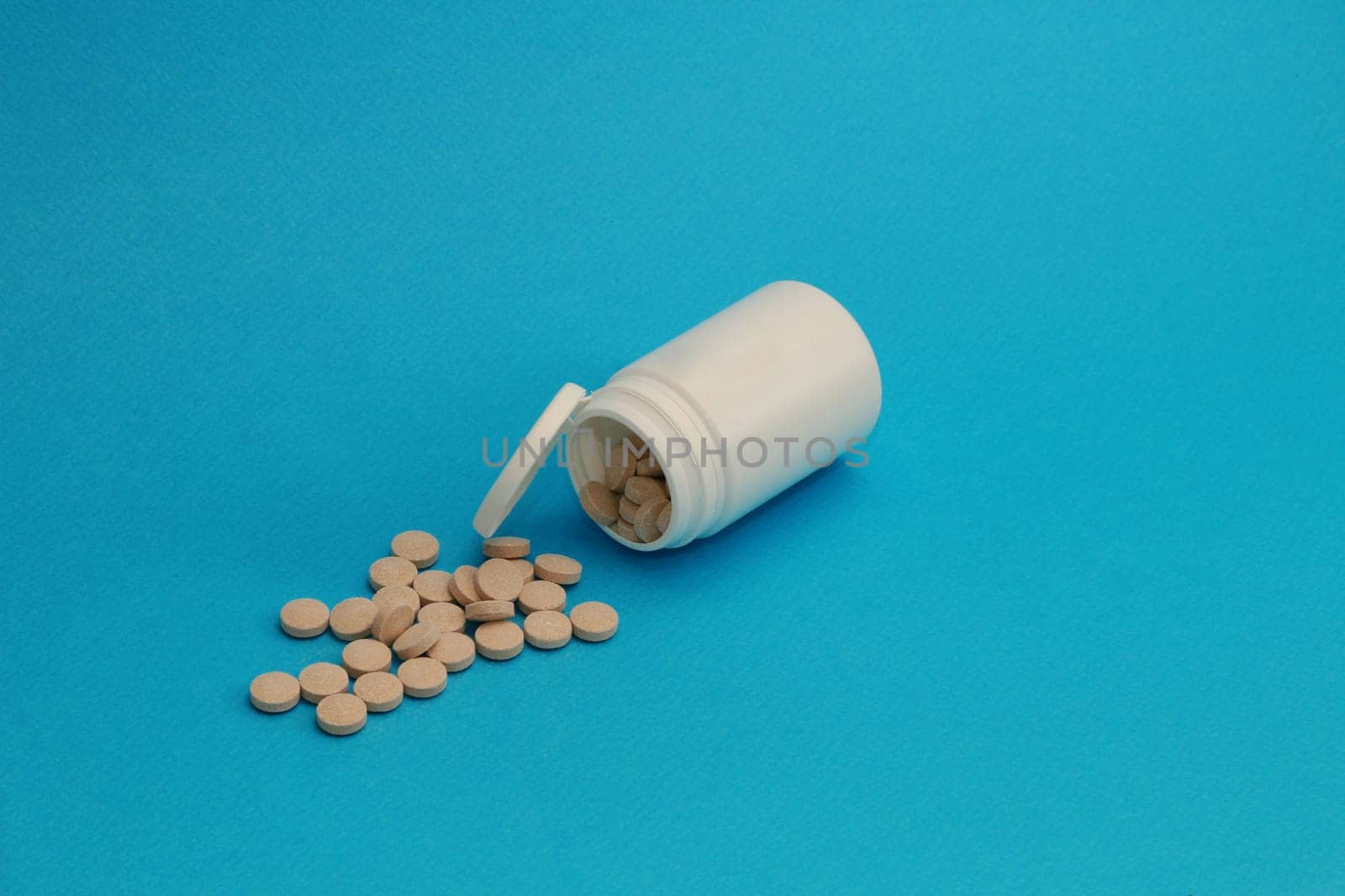 Medicine and health concept. Close up of teblets pills spilling from Plastic pill bottle on blue background with selective focus.