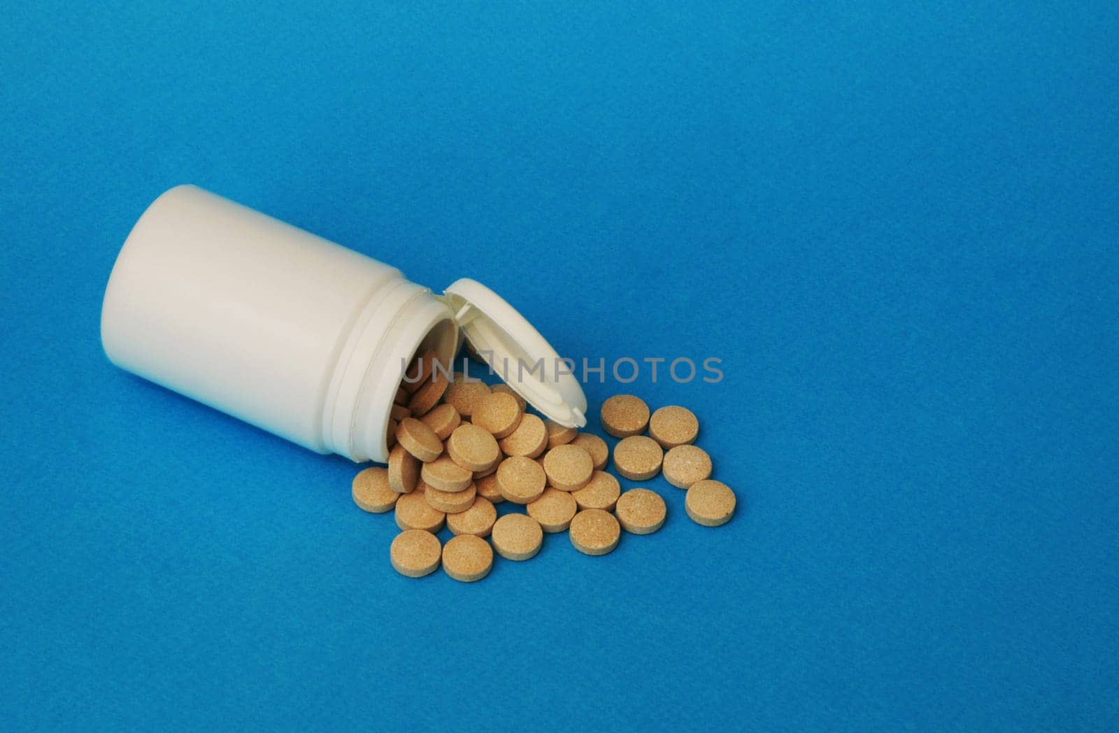 Brown pills and a white jar on a blue background. by gelog67