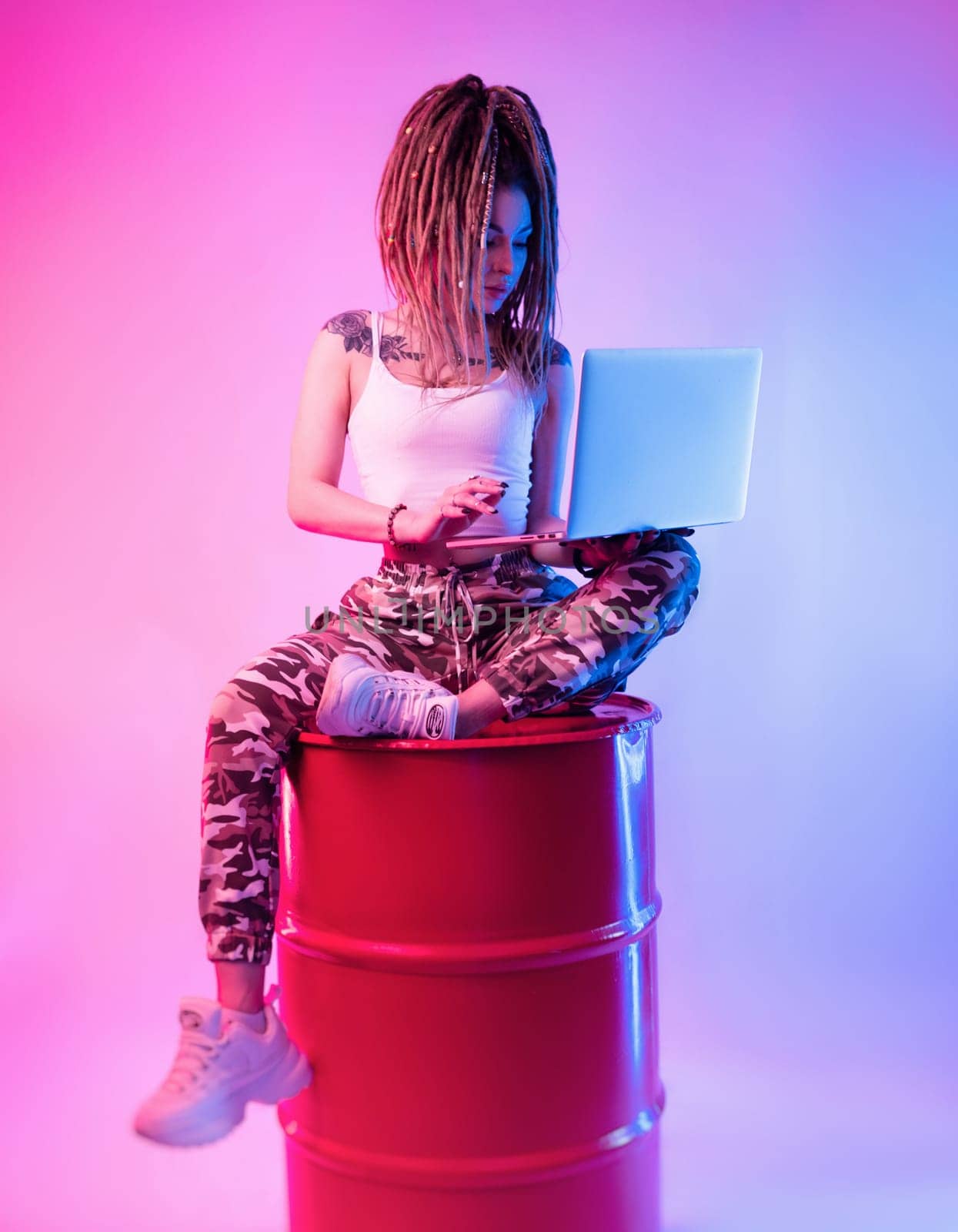 sexy girl with braids dreadlocks on her head in neon light with a laptop on a light background copy paste