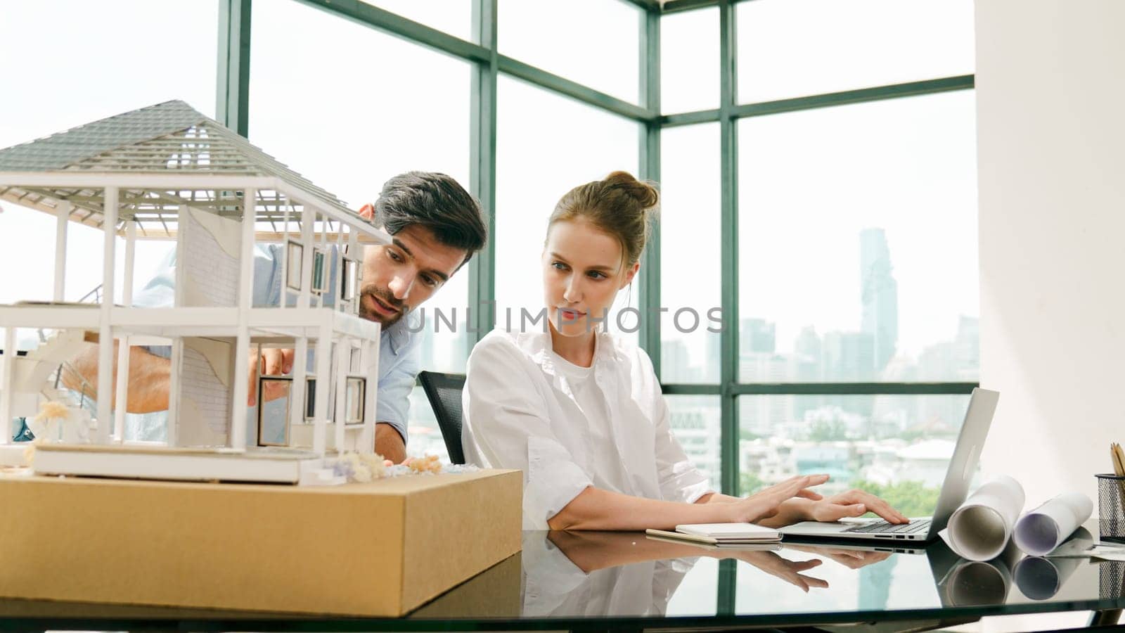 Smart architect engineer inspect house model while colleague using laptop analysis data. Professional designer team working together to design house model construction at modern office. Tracery