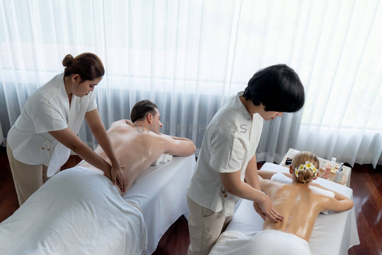 Caucasian couple customer enjoying relaxing anti-stress spa massage and pampering with beauty skin recreation leisure in day light ambient salon spa at luxury resort or hotel. Quiescent